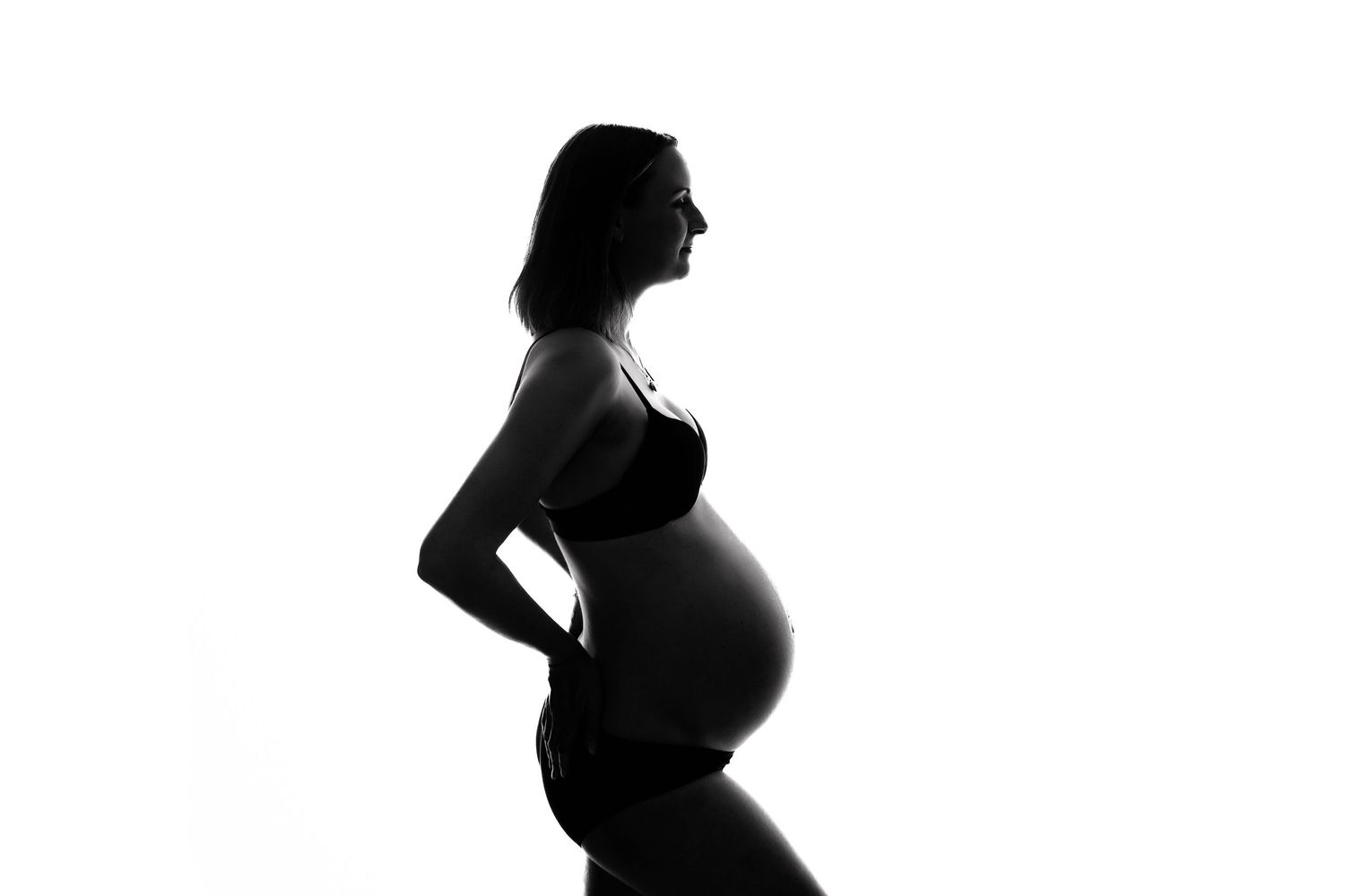 Black and white silhouette of a pregnant woman standing sideways against a white background.