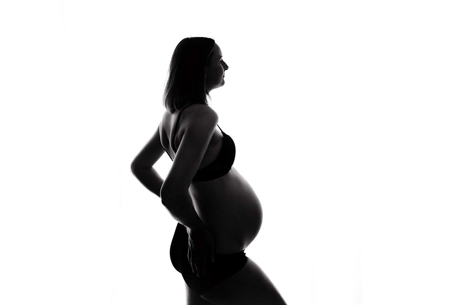 Black and white silhouette of a pregnant woman posing sideways, showcasing her baby bump against a white background.