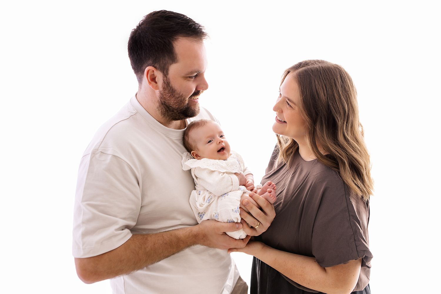 Happy parents smiling at their laughing newborn baby against a white studio background.