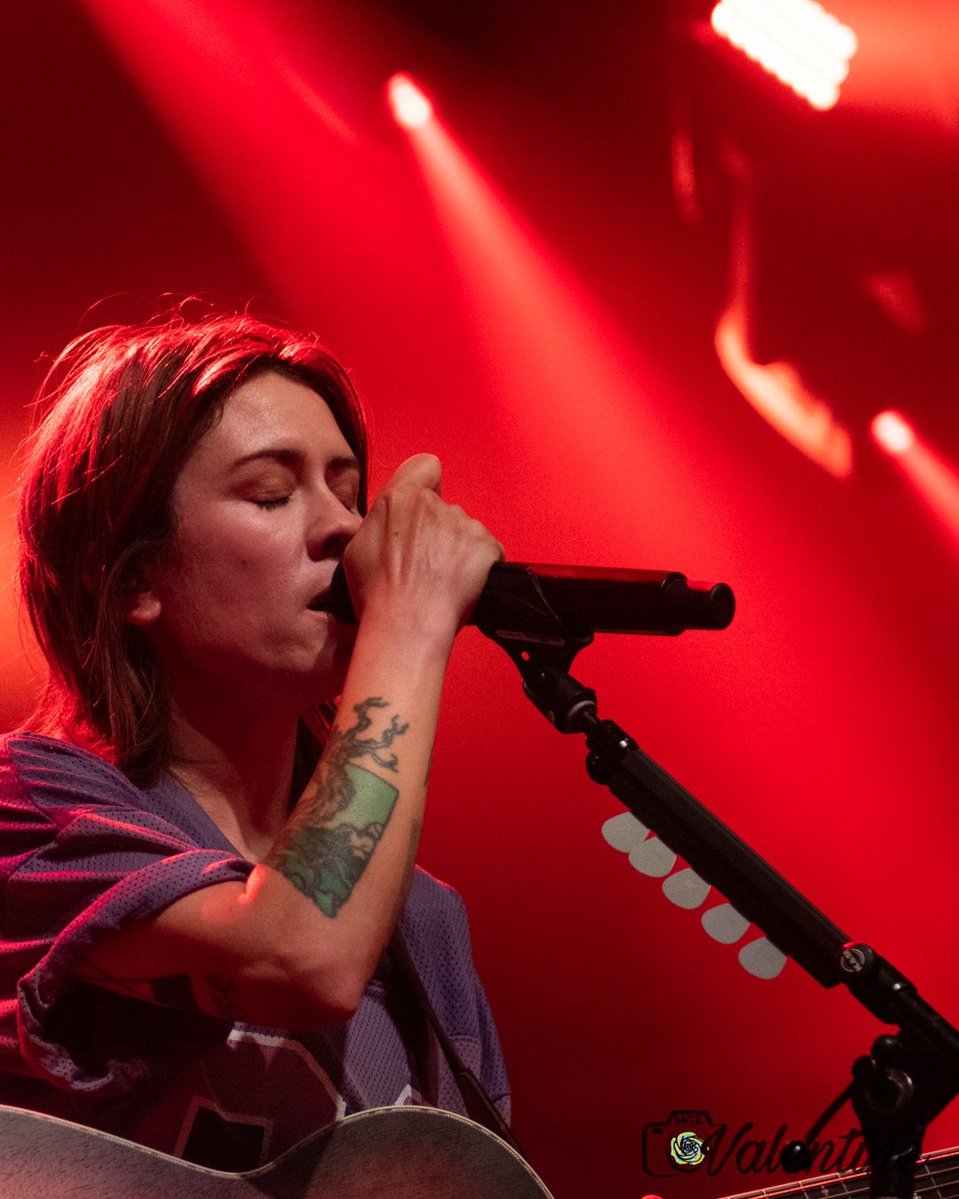 Singer performing on stage with dramatic red lighting effects.
