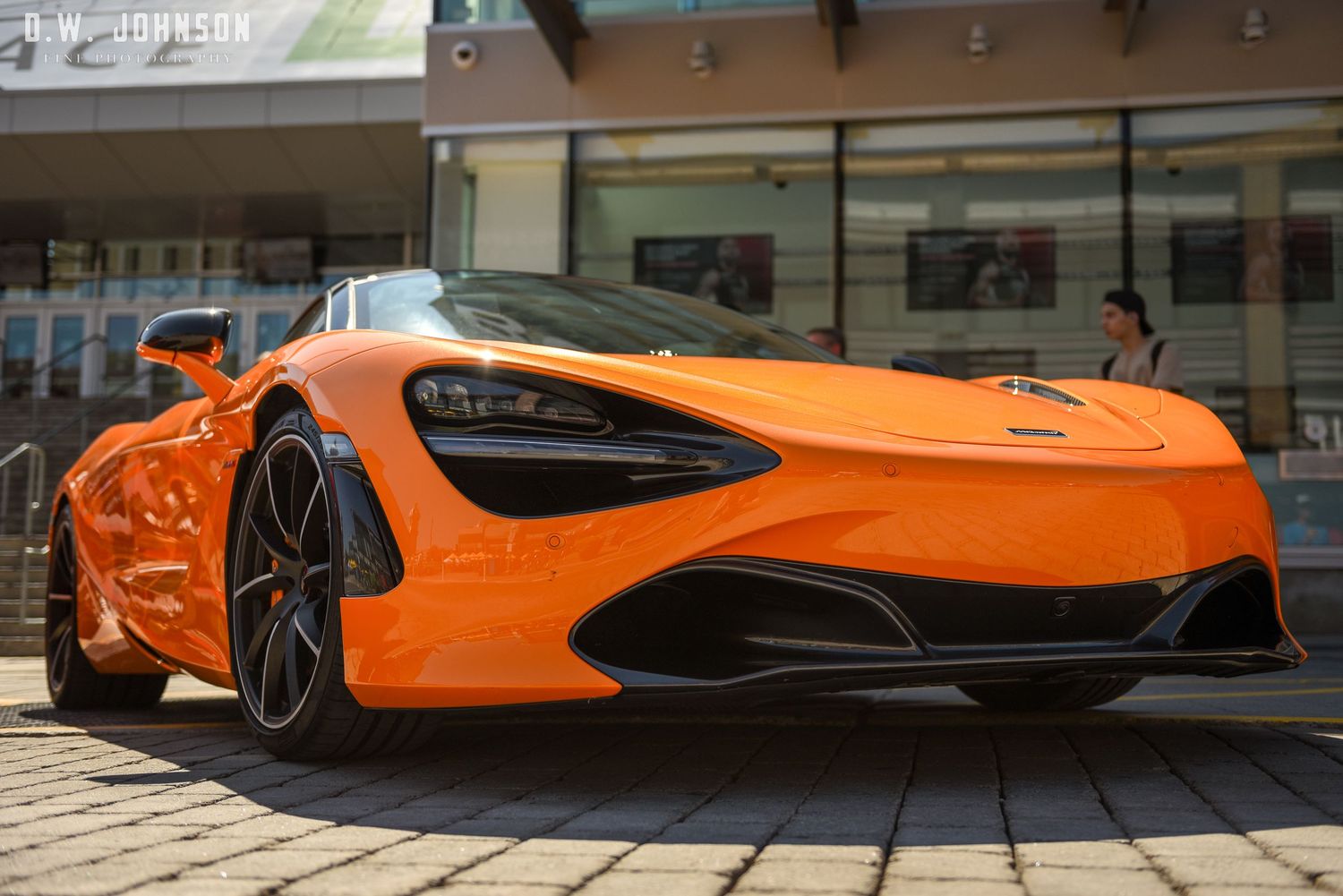 A vibrant orange McLaren 720S supercar on display outside a shopping center.