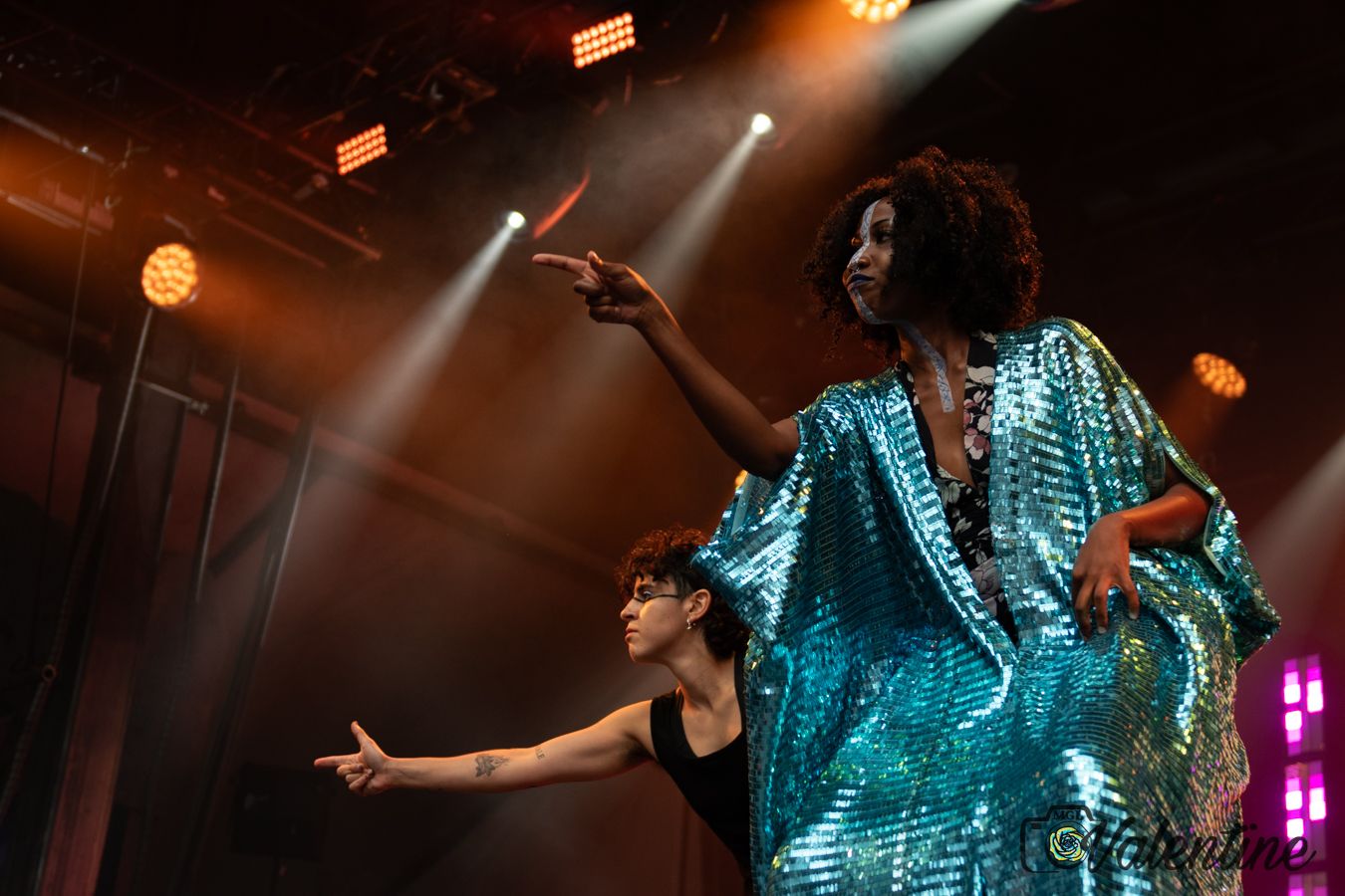 Performer in sparkly turquoise costume dancing under dramatic stage lighting.