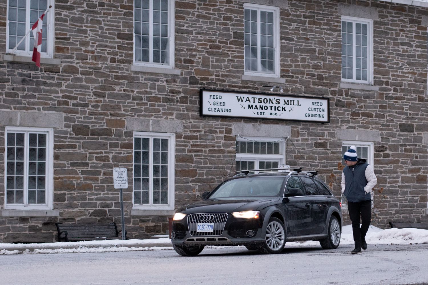 A snowy winter scene outside a historic stone building with parked cars and a person walking in Quebec City.