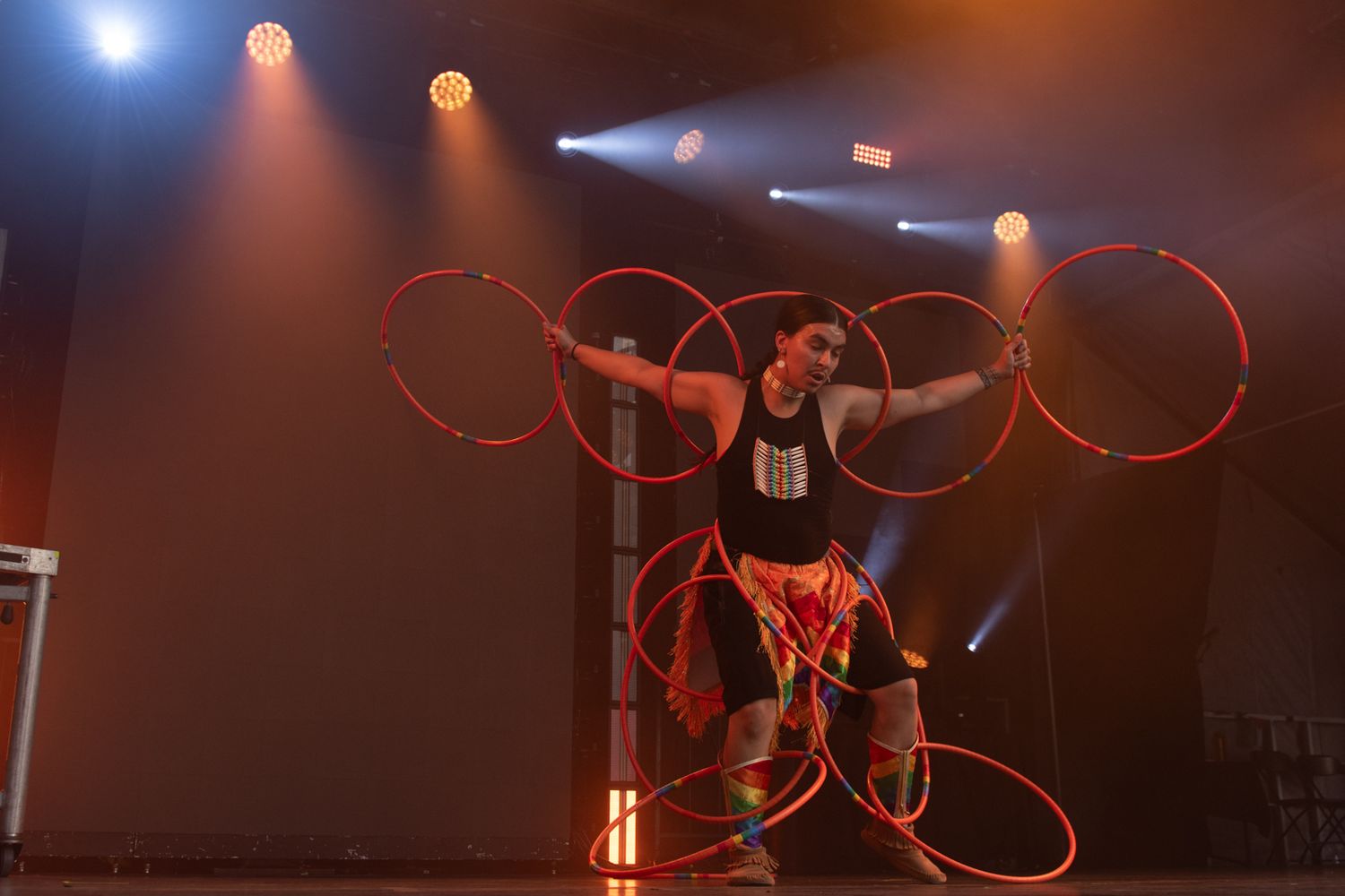 A gymnast performs with a red ribbon during a rhythmic gymnastics routine under dramatic stage lighting.