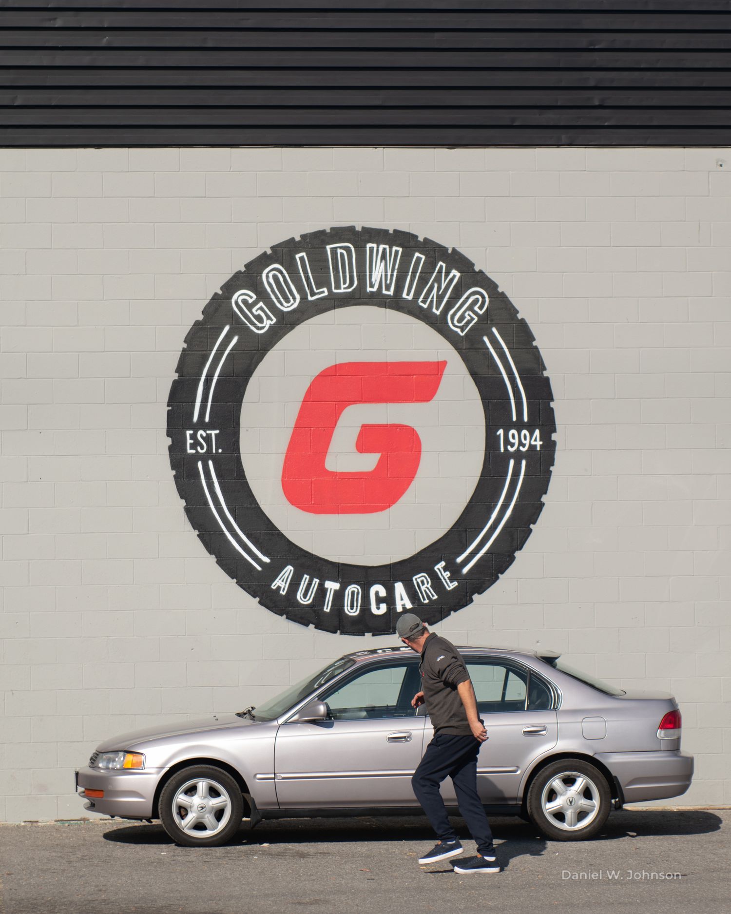 A sedan parked in front of a Goldwing Autocare logo painted on a white wall.