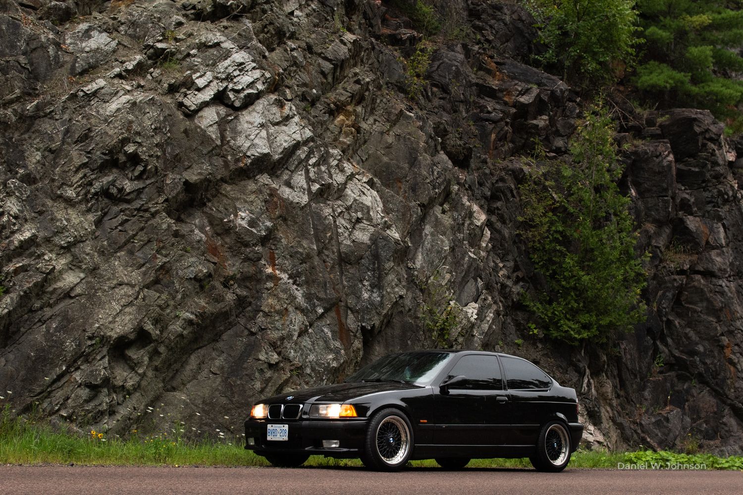 Black sports cars parked against rocky mountain cliff face.