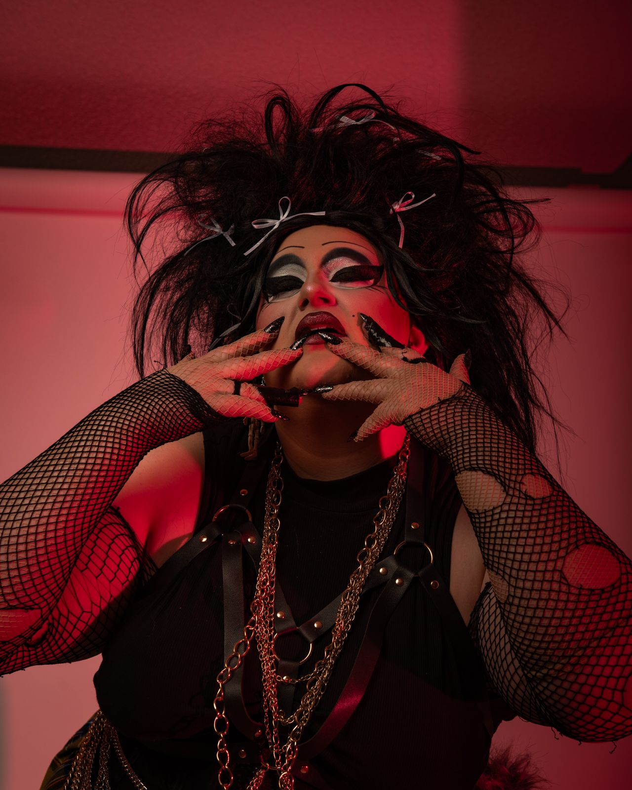 A dramatic portrait series in dark red lighting shows a figure in fishnet and chains with expressive poses and gestures.