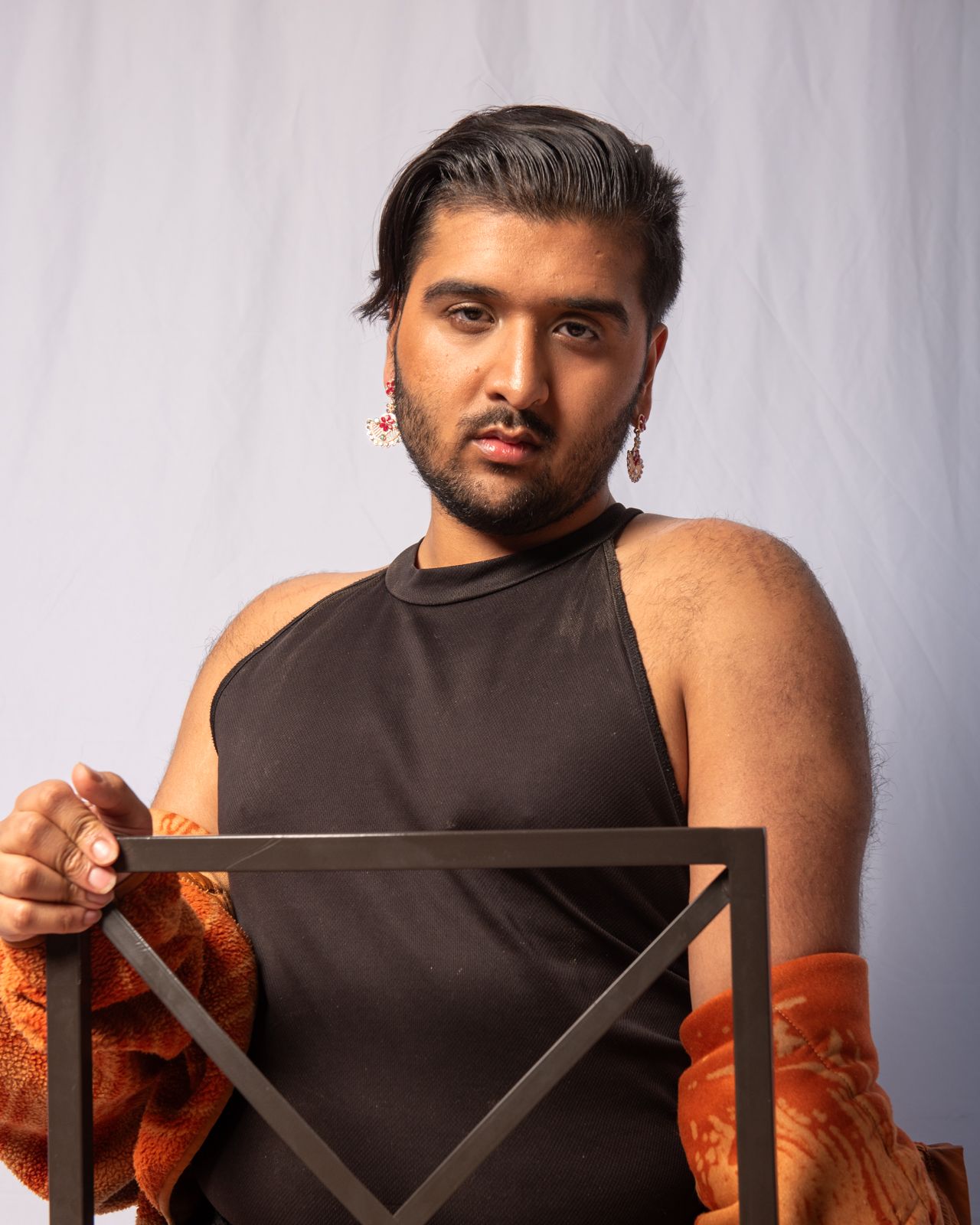A person in black sleeveless attire poses with geometric wooden frames against a gray studio backdrop.