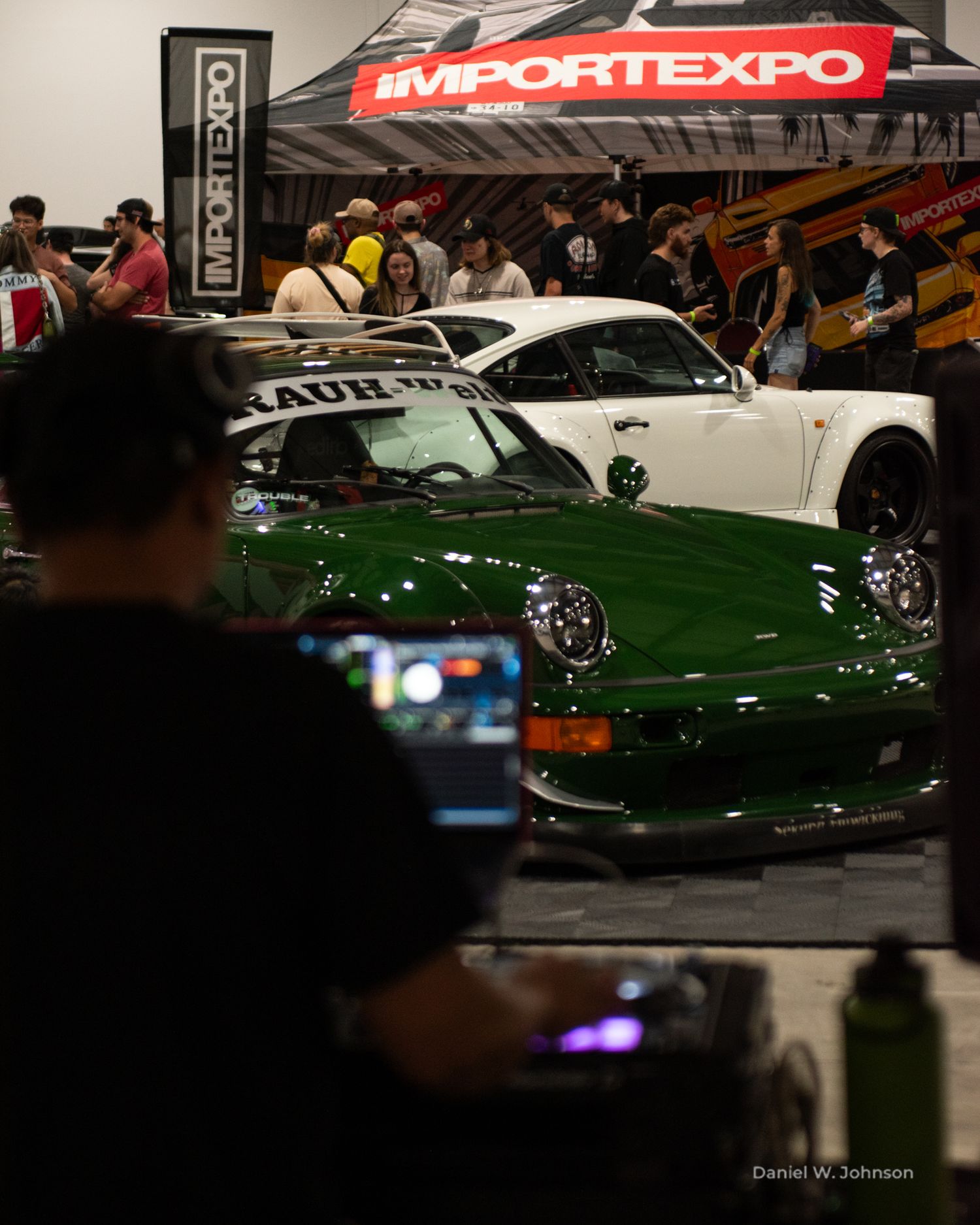 Classic cars on display at an indoor auto expo show with red banners and signage.