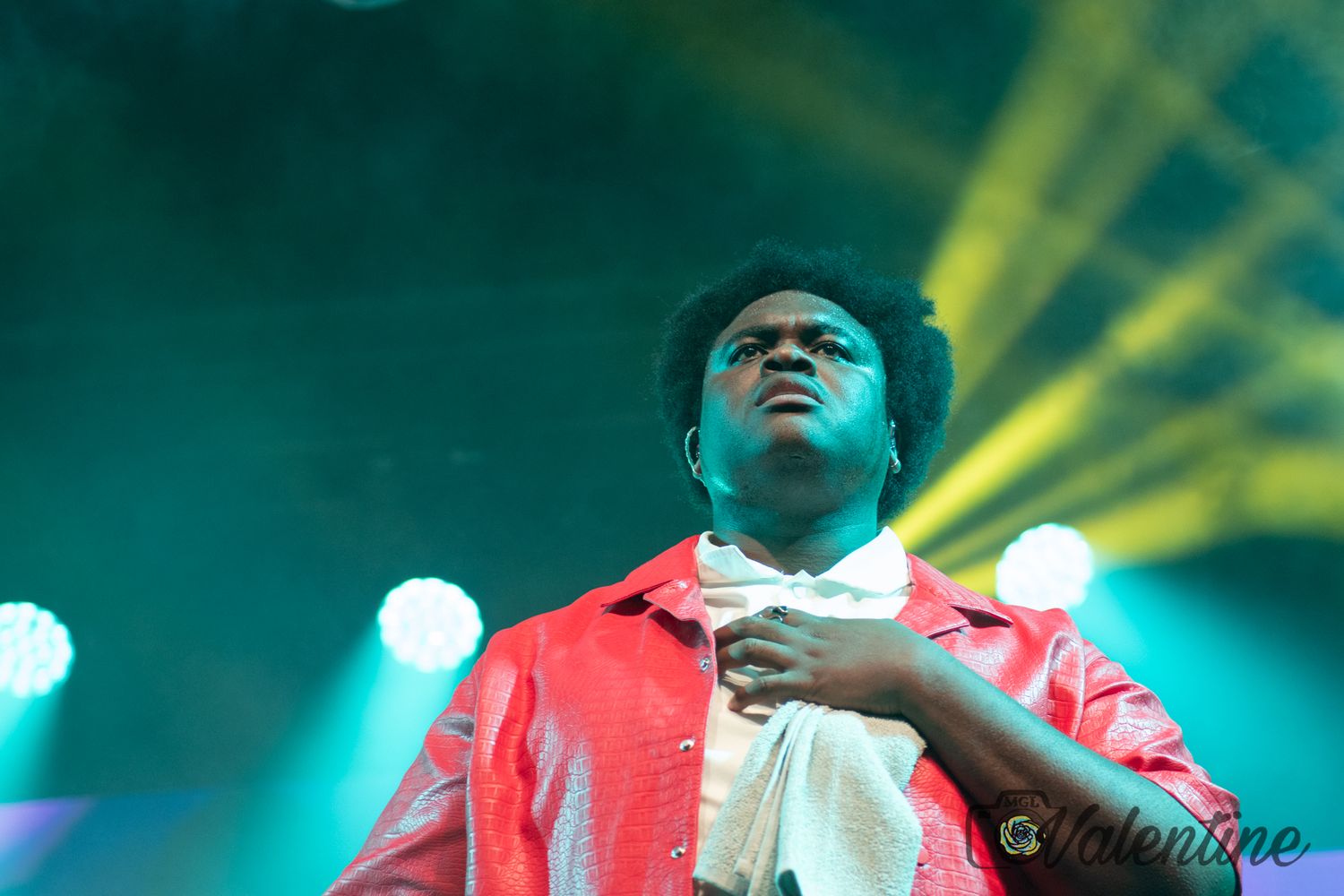 Concert performer in red jacket under dramatic green and yellow stage lighting.