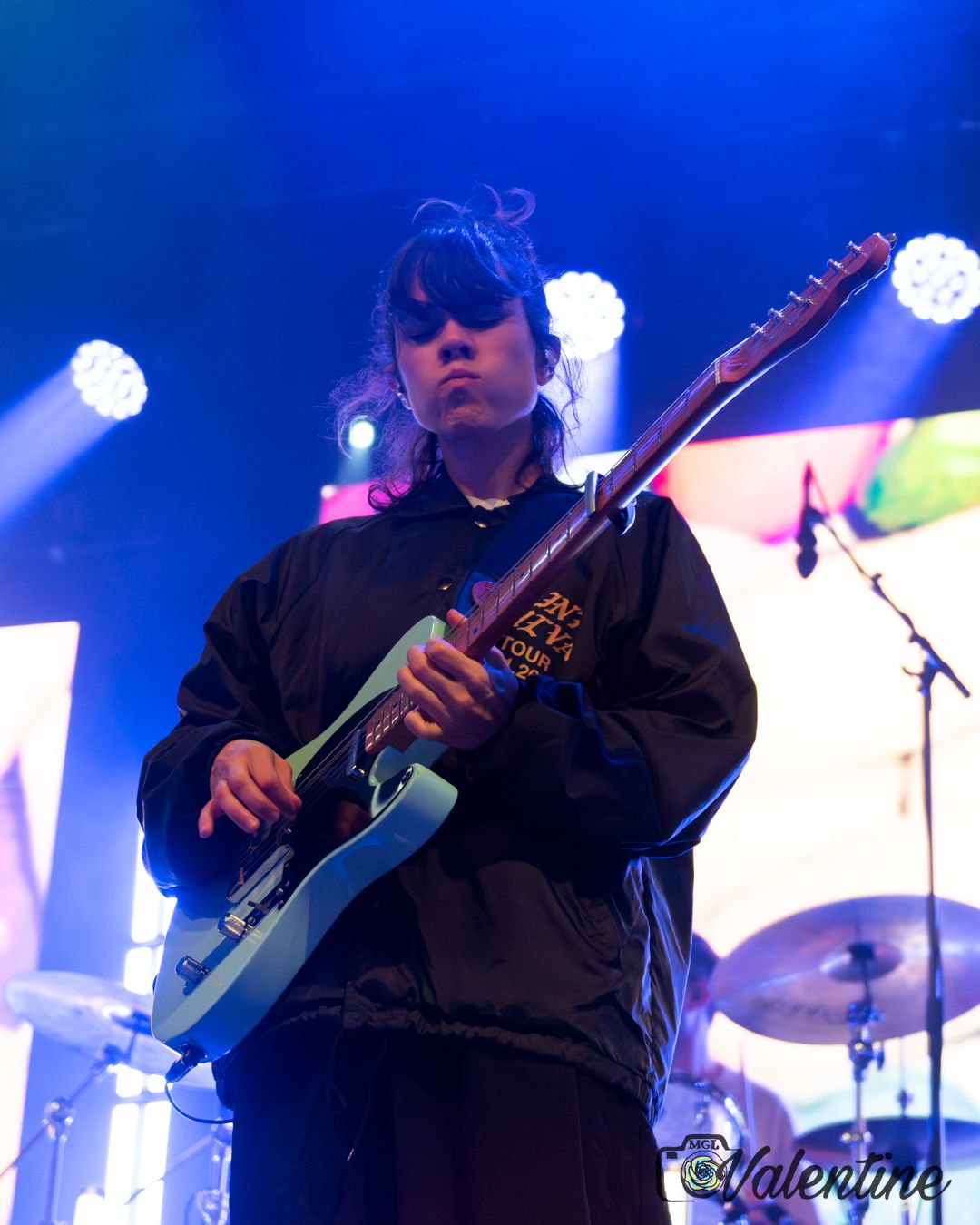 Musician performing on electric guitar with blue stage lighting and spotlights.