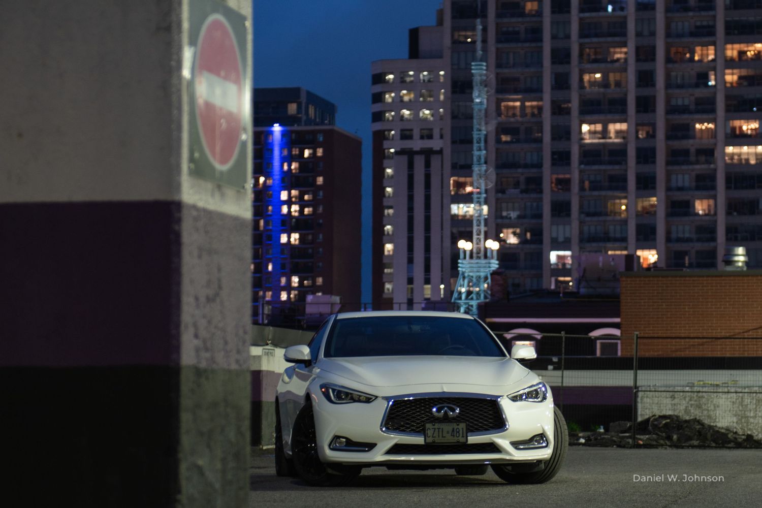 A white Infiniti Q50 parked in an urban setting during blue hour with city lights in background.