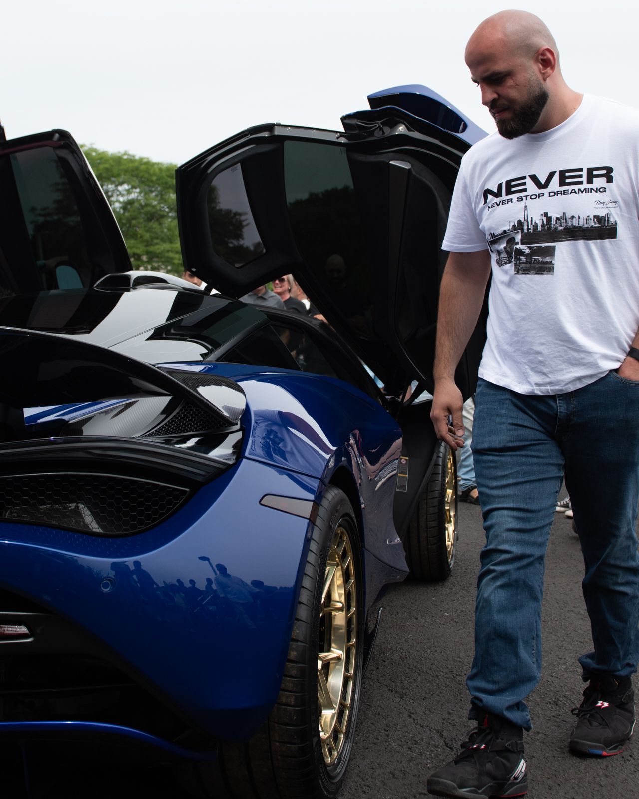 Blue sports car with gold wheels being inspected in a parking lot.