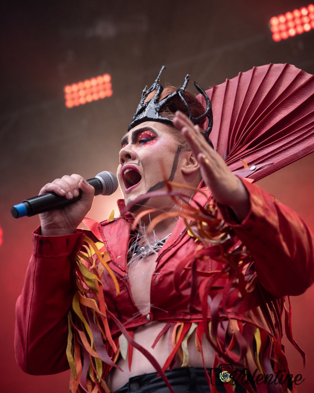 Dramatic stage performance with performer in red costume and ornate headpiece.