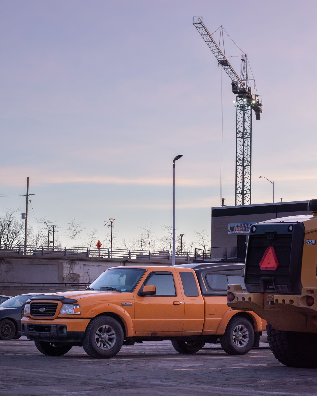 Orange pickup truck parked in an industrial area with construction equipment.