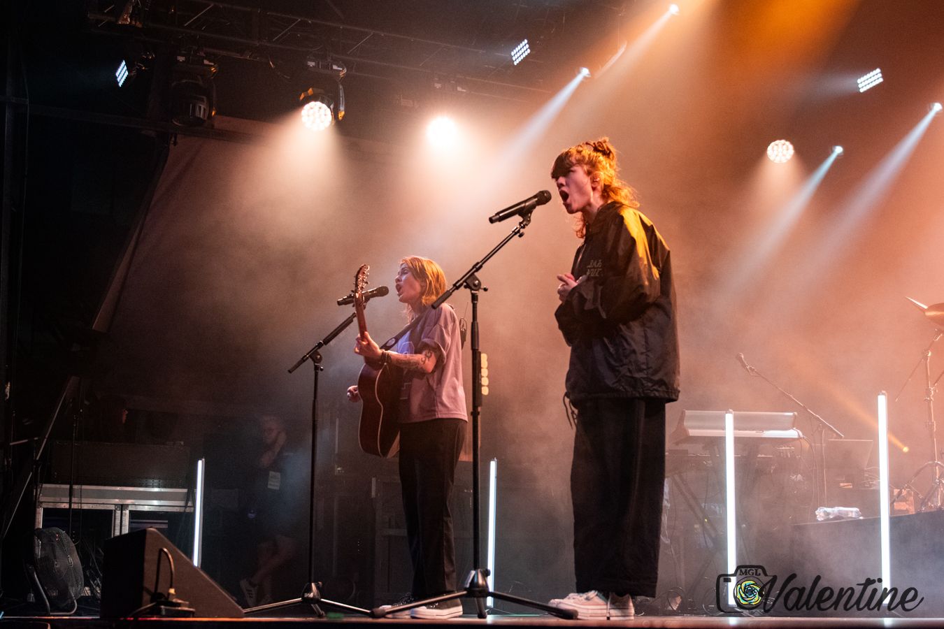 Musicians performing on stage with dramatic orange lighting and fog effects.