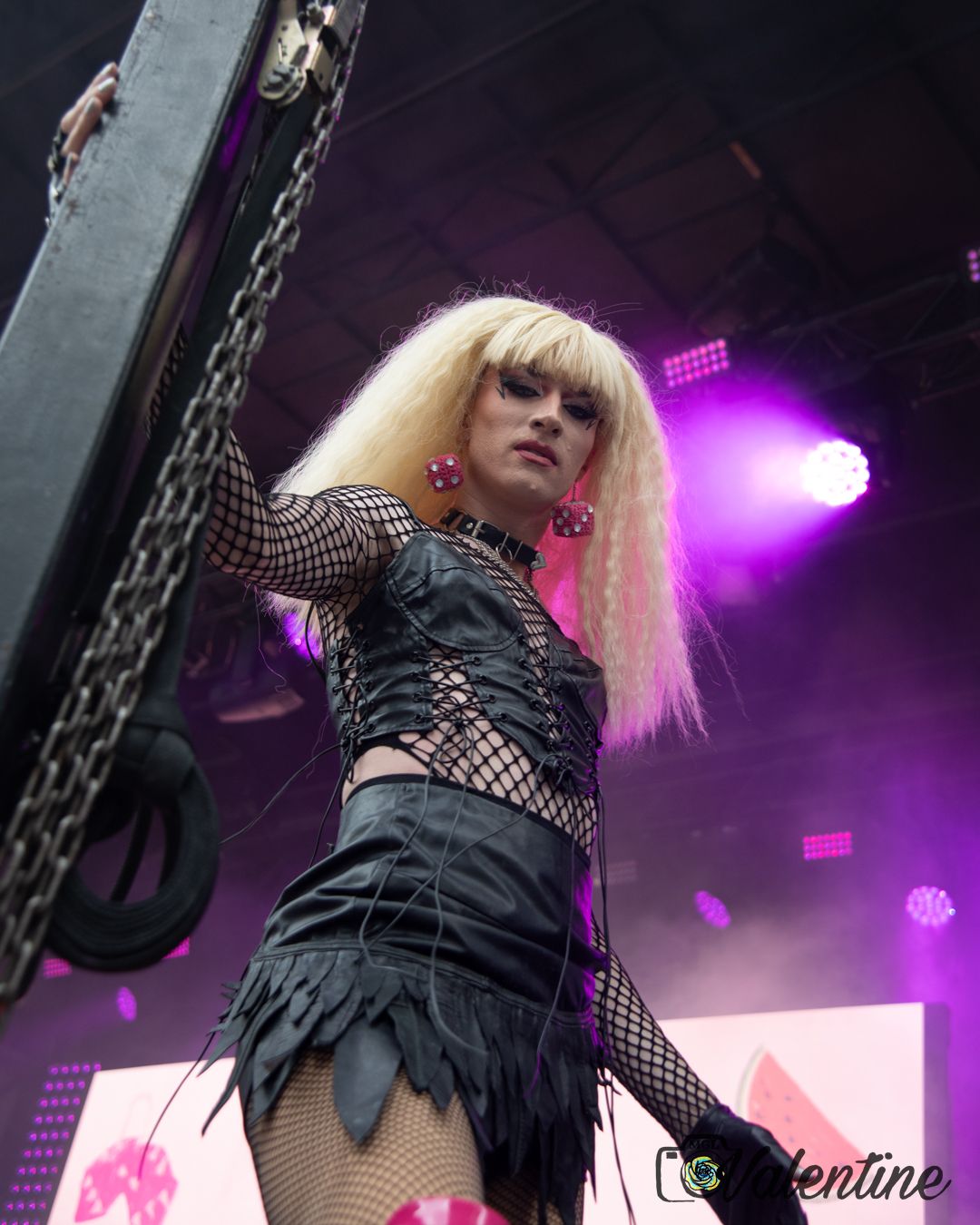 Performer in black costume and fishnet stockings dances on stage with dramatic purple lighting effects in background.