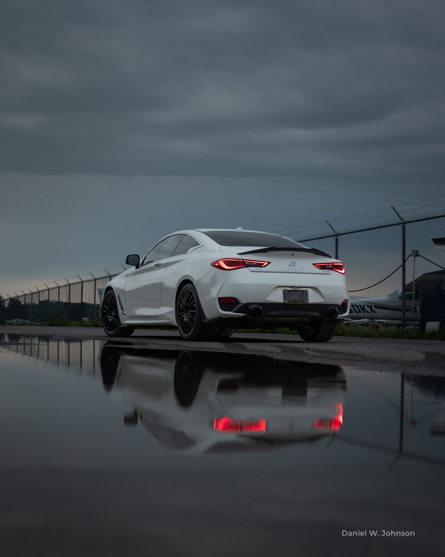 A white BMW M4 car is reflected in still water under moody dark clouds at dusk.