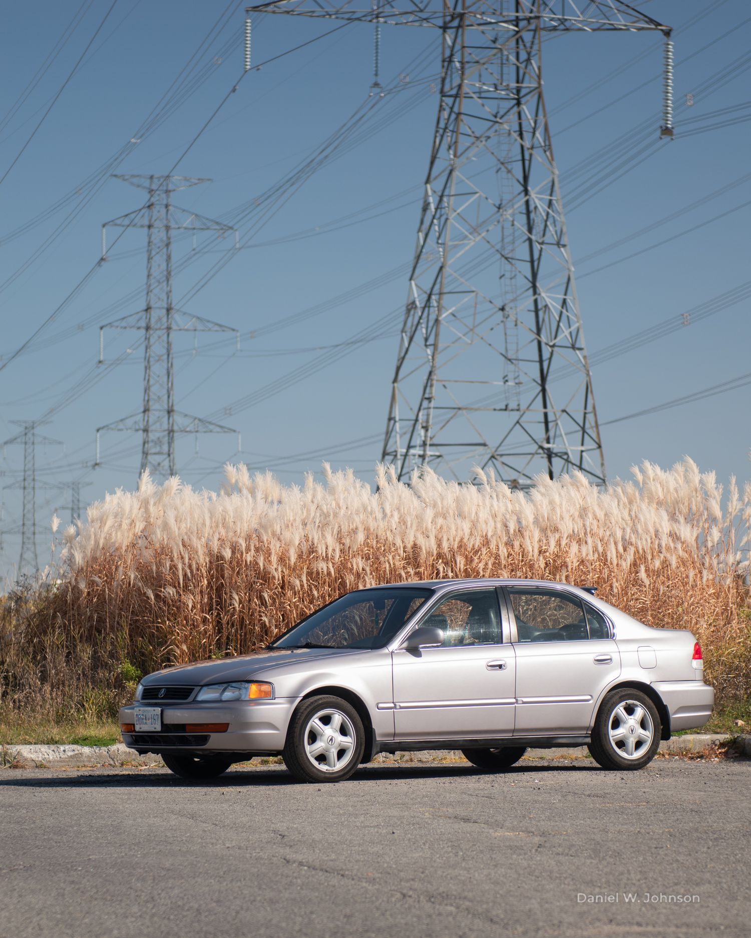 A sedan parked near power transmission towers and tall grass.