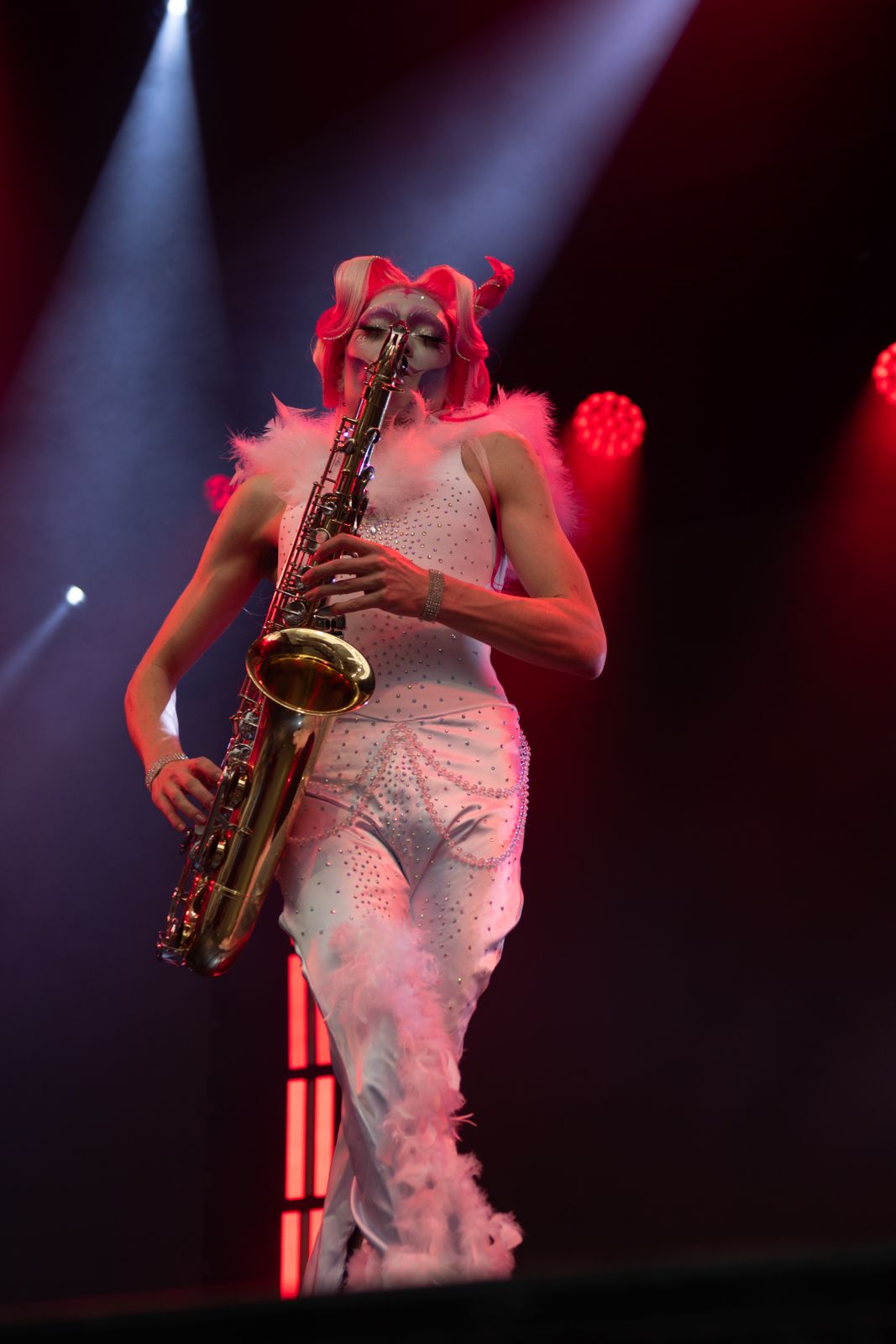A musician performs on stage with a saxophone under dramatic red and blue lighting.
