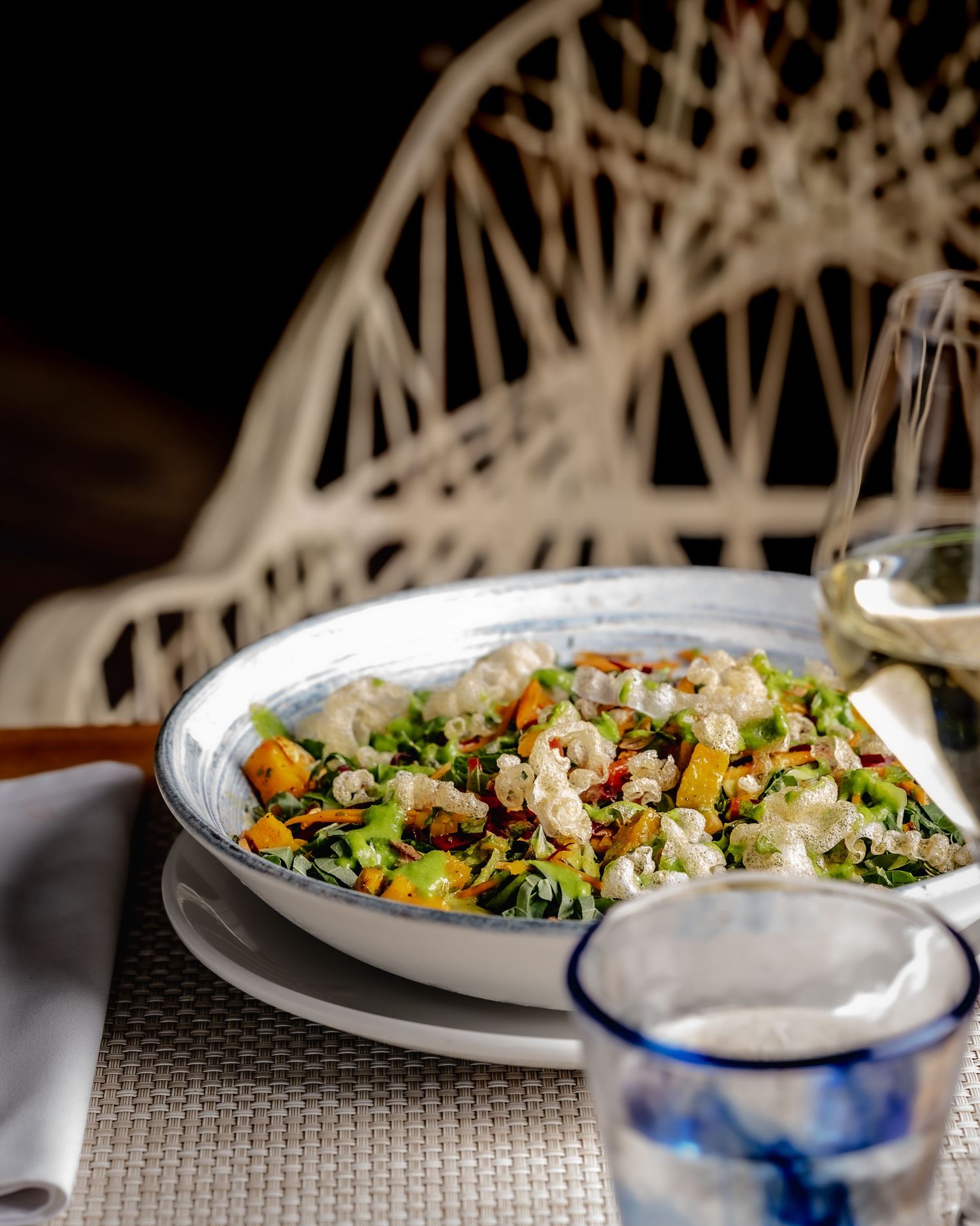 Fresh garden salad with roasted vegetables, crumbled cheese, and herbs served in a white bowl at an elegant restaurant.