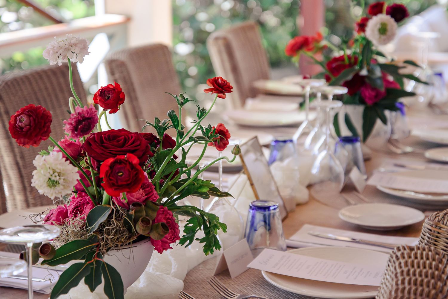 Elegant wedding reception tables decorated with deep red floral centerpieces and white place settings.
