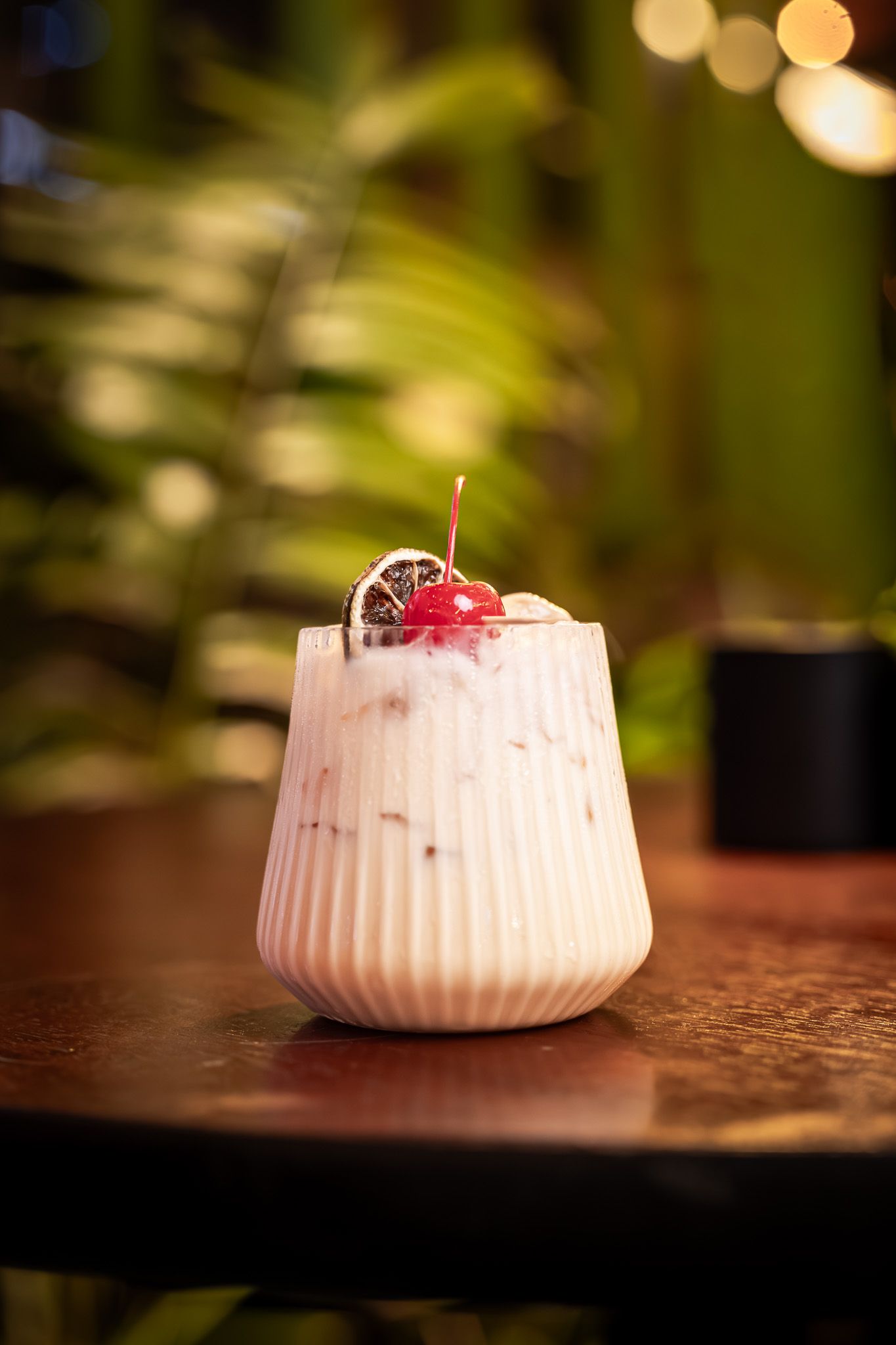 A creamy white dessert mousse topped with fresh cherries served in a small ruffled ceramic bowl.