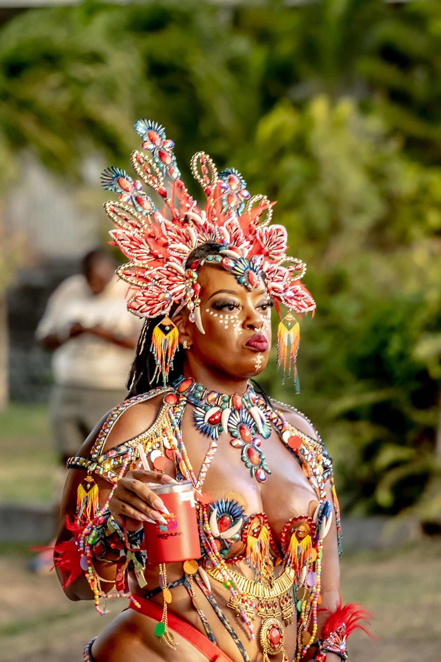 Woman in vibrant carnival costume with ornate feathered headdress and beaded outfit at a tropical festival.