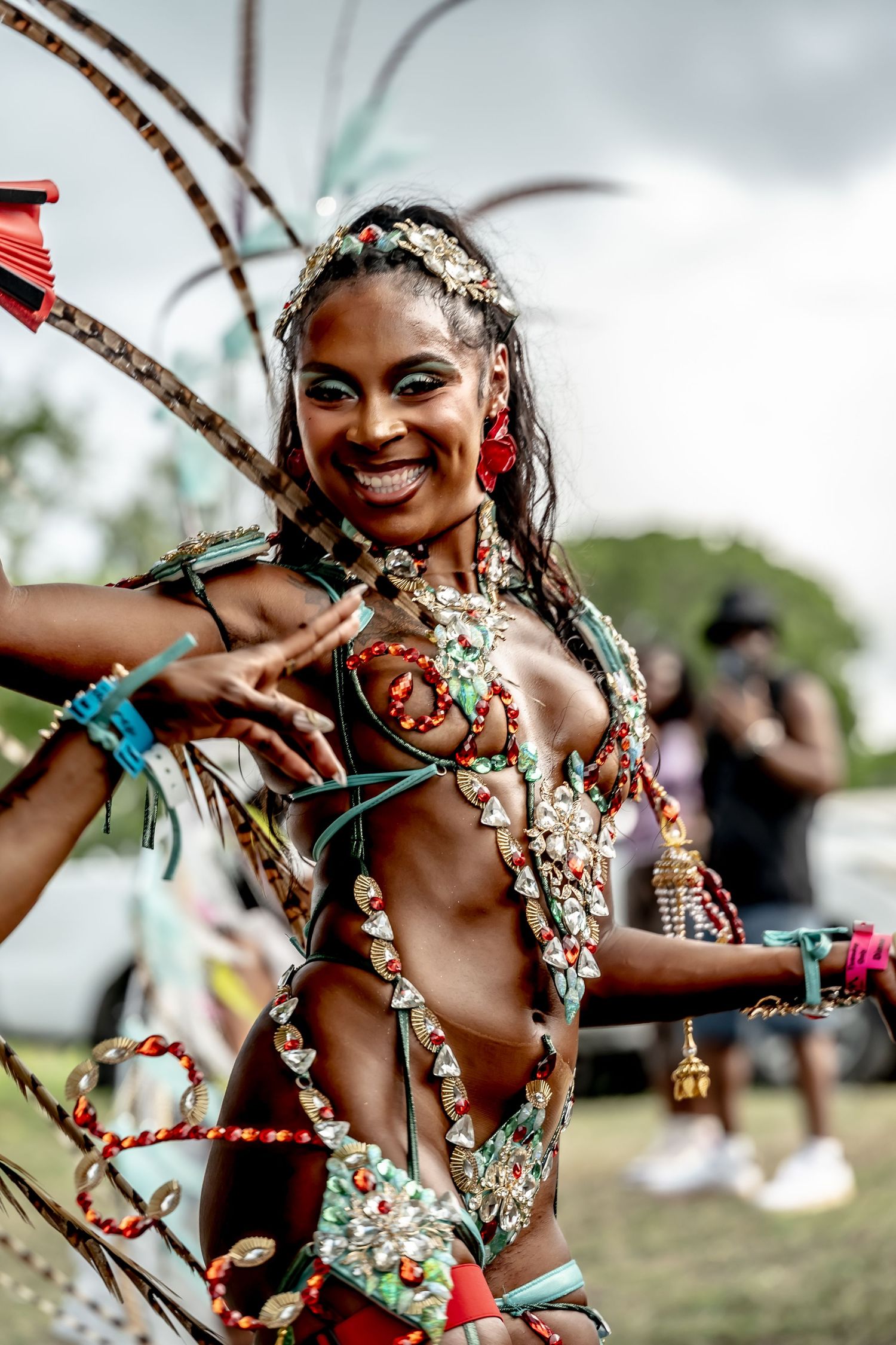 Smiling woman in vibrant carnival costume with ornate beaded bikini and feathered headdress at outdoor festival.