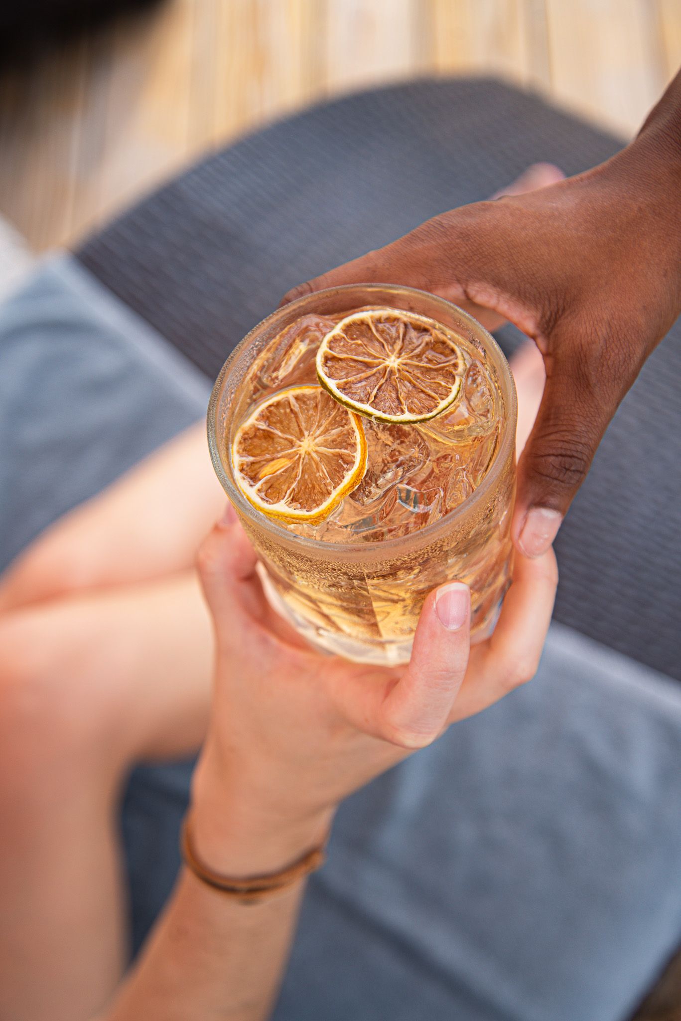 A hand holds a clear glass filled with pink liquid and garnished with dried orange slices.