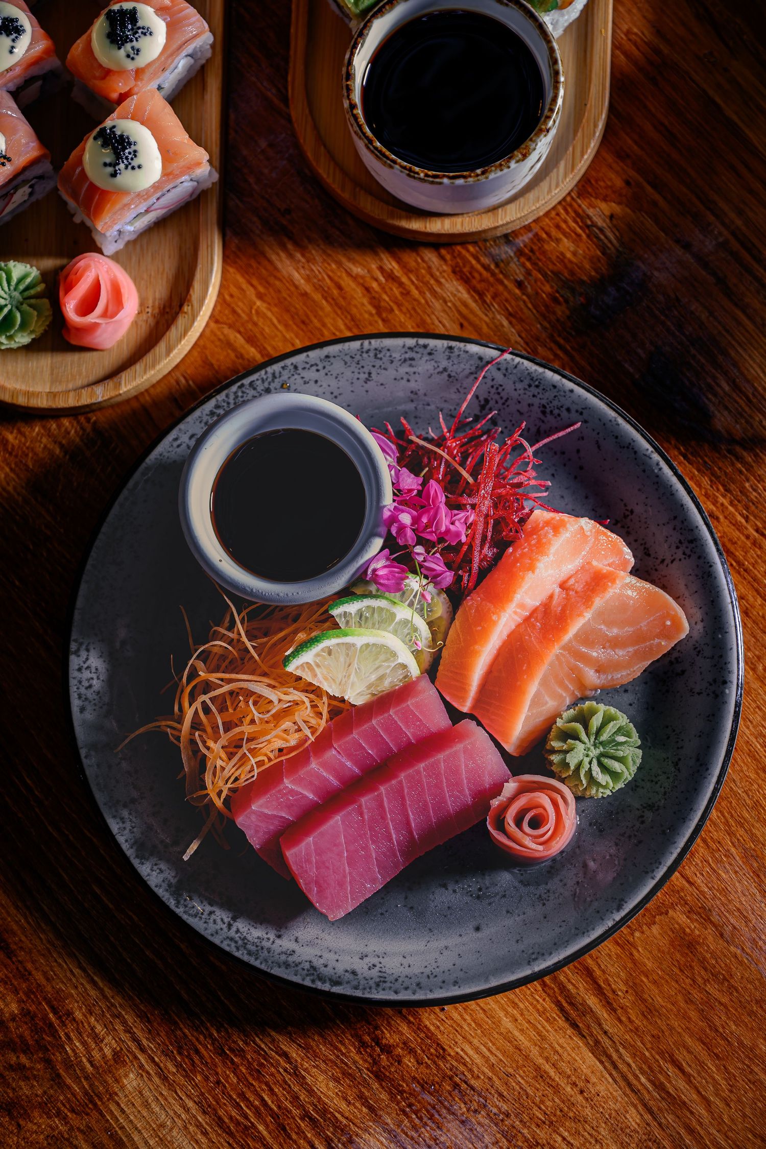 Elegant sashimi platter with fresh tuna and salmon slices, wasabi, lime, and soy sauce on a dark ceramic plate.
