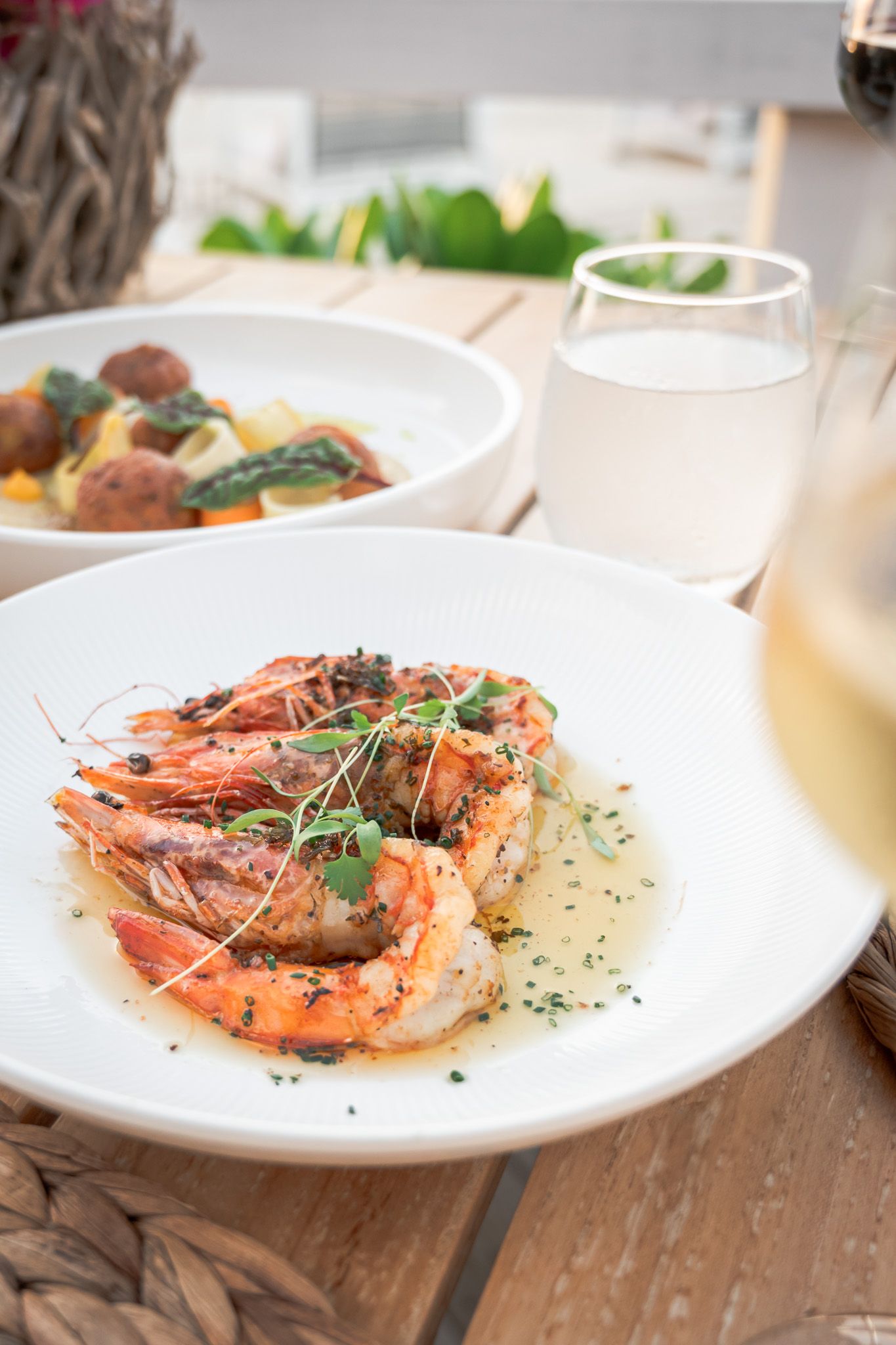 Grilled shrimp garnished with fresh herbs served on white plates at an elegant restaurant setting.