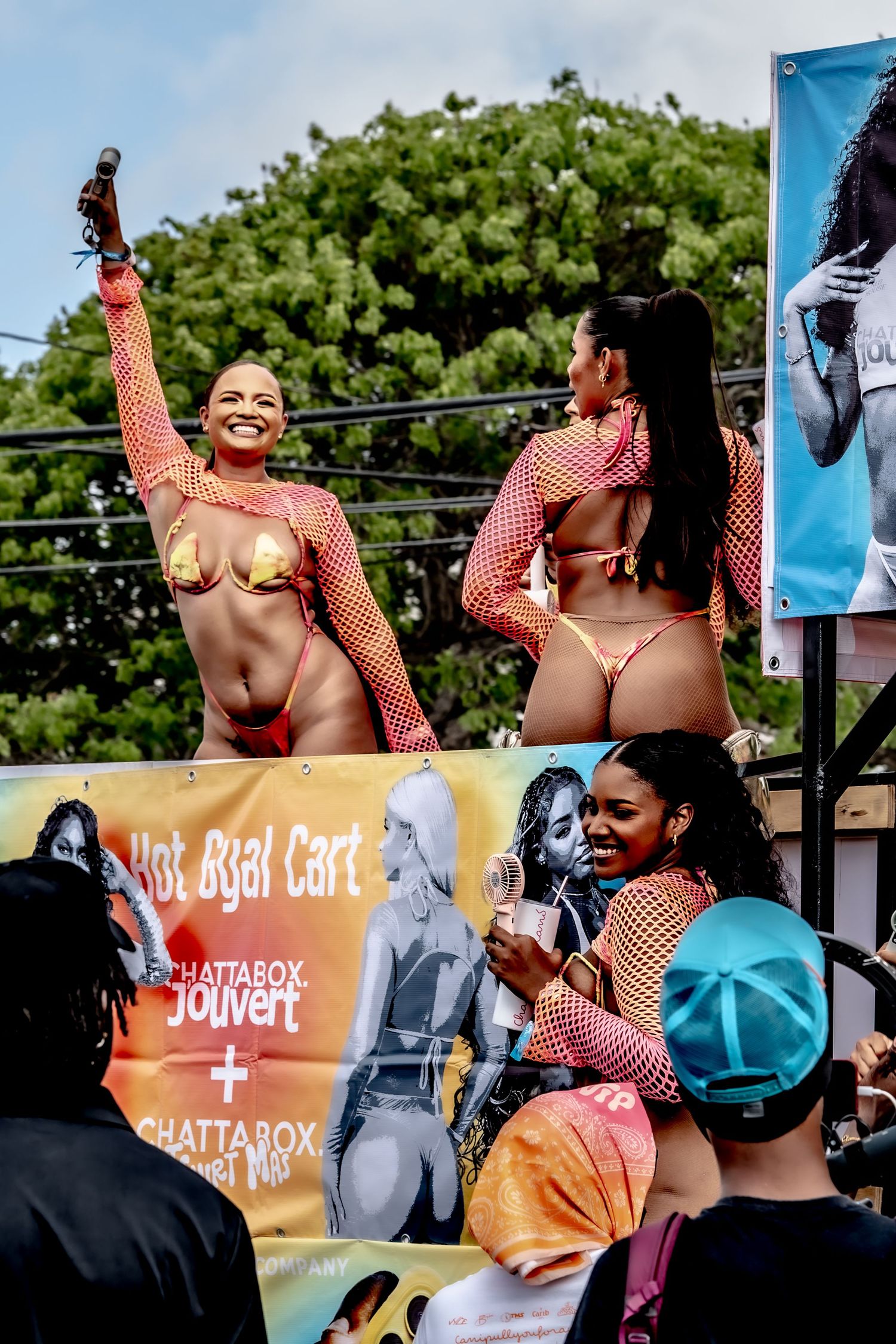 Women in colorful festival costumes performing on stage at a Caribbean Jouvert celebration with crowd below.