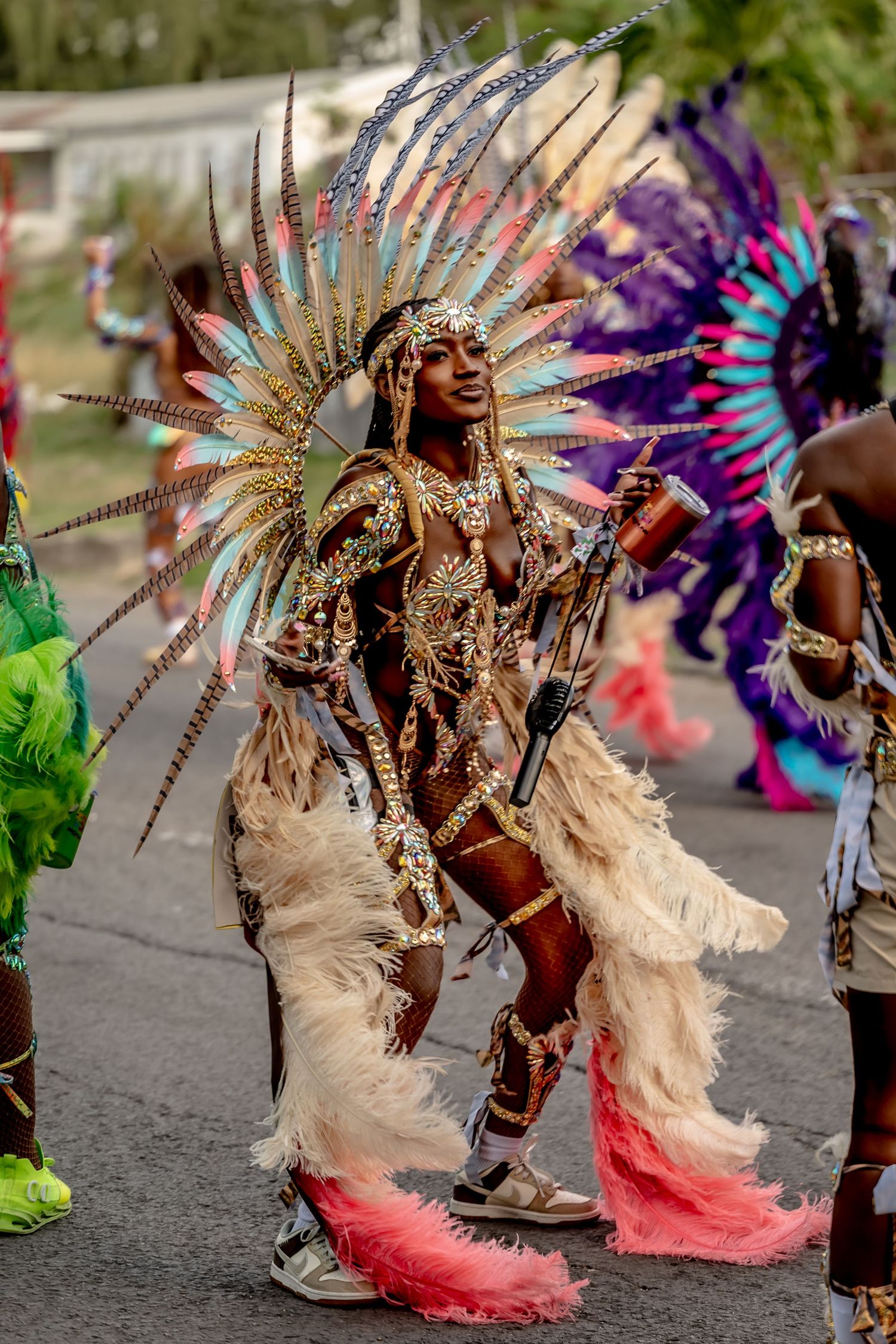 Vibrant carnival dancer in elaborate gold feathered costume performs on street during colorful Caribbean festival parade.