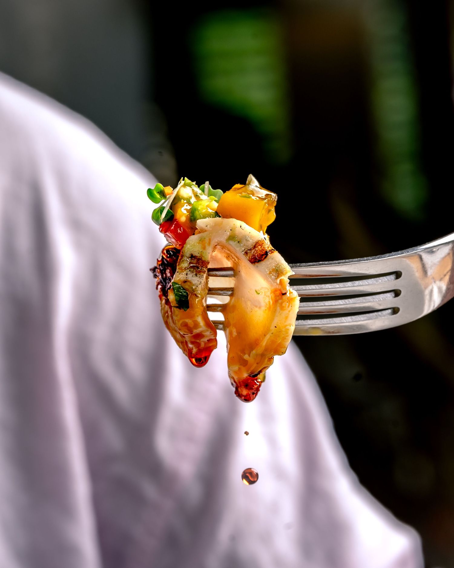 A fork holding colorful pasta with vegetables and sauce, held by a chef in a white uniform.