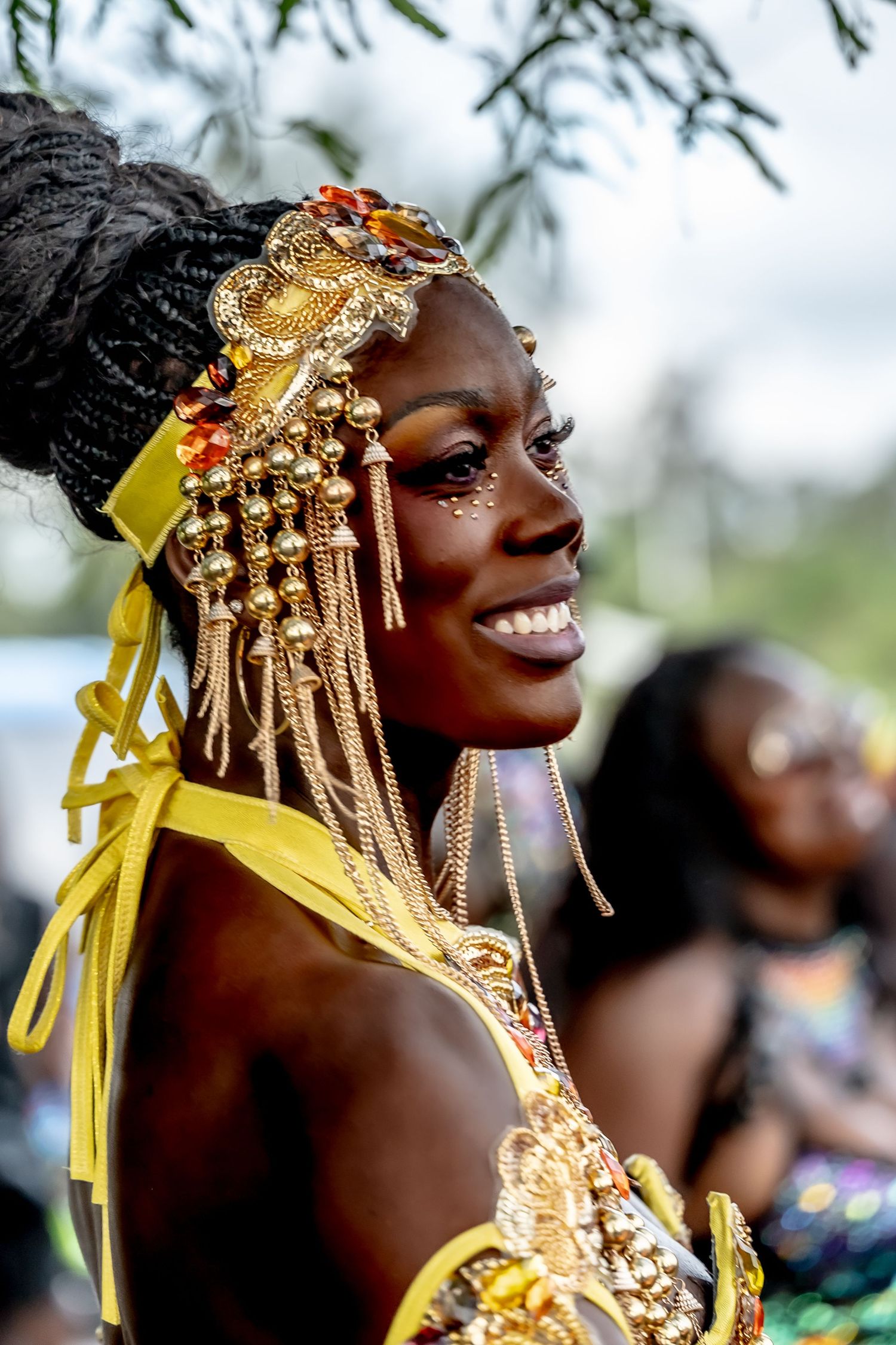 Smiling woman in gold carnival costume with ornate headdress and yellow ribbons at a cultural festival.