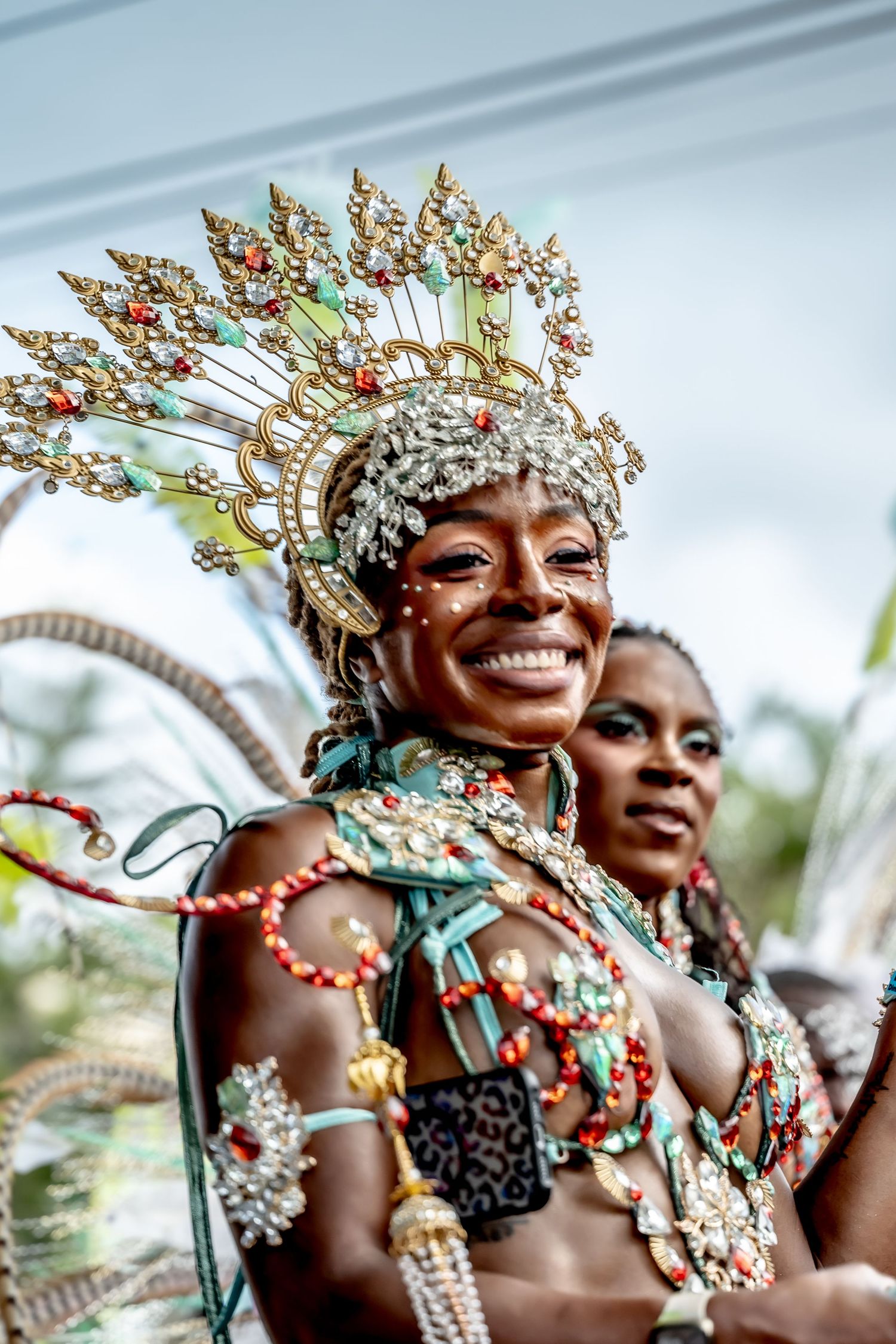 Smiling woman in ornate golden carnival headdress and colorful beaded costume at a vibrant festival celebration.