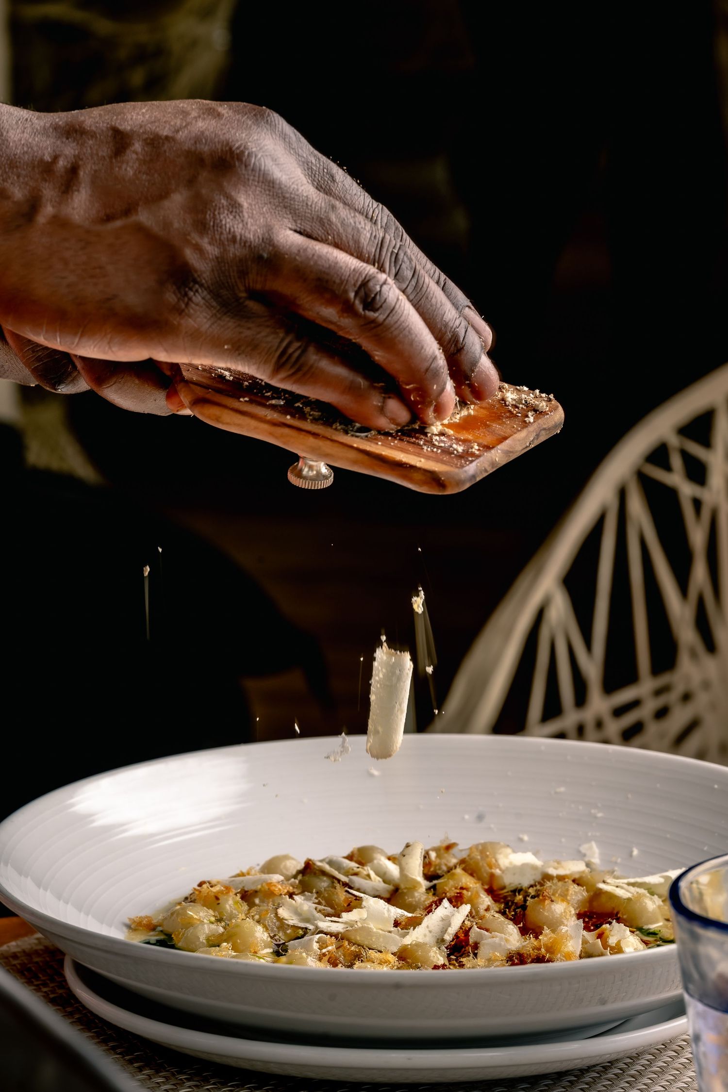 Chef grating fresh Parmesan cheese over a gourmet pasta dish in a white bowl at an upscale restaurant.