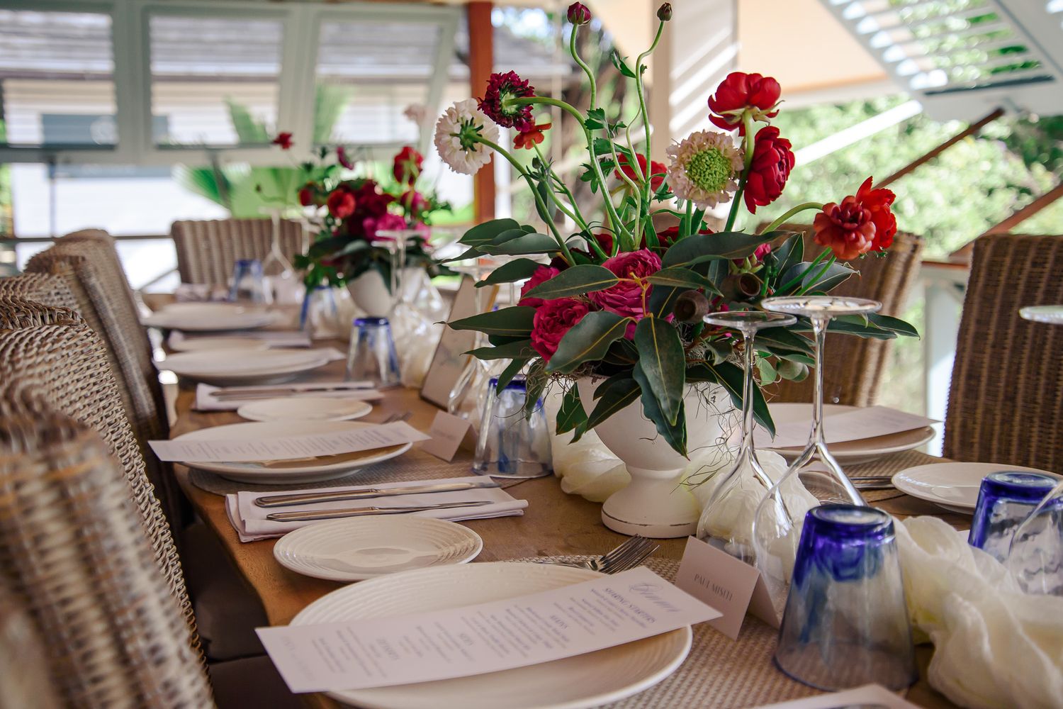 Elegant table settings with red floral centerpieces and white plates arranged for a formal dining event.