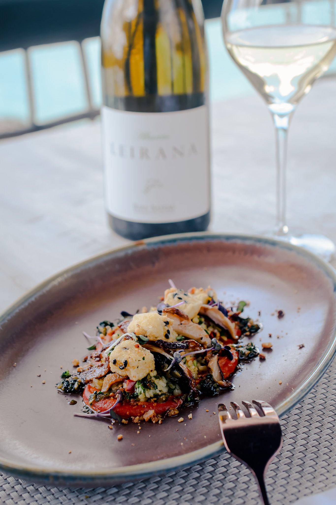 Elegant plated seafood dish with black rice and colorful garnishes served on rustic ceramic plates with wine glasses.