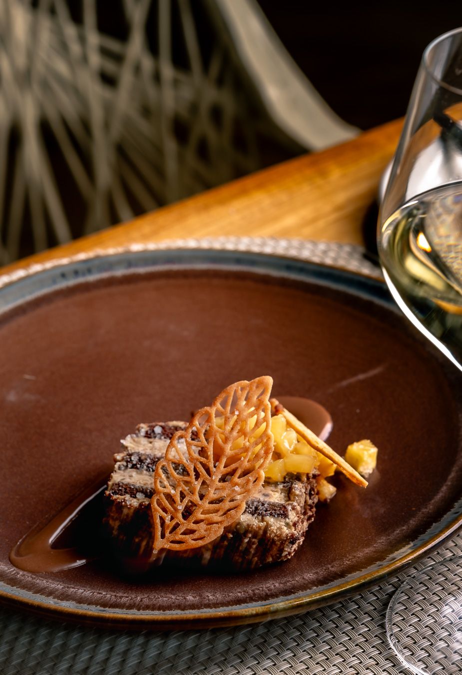 Elegant fine dining dish with braised meat, caramel lattice garnish, and rich sauce on a dark ceramic plate.