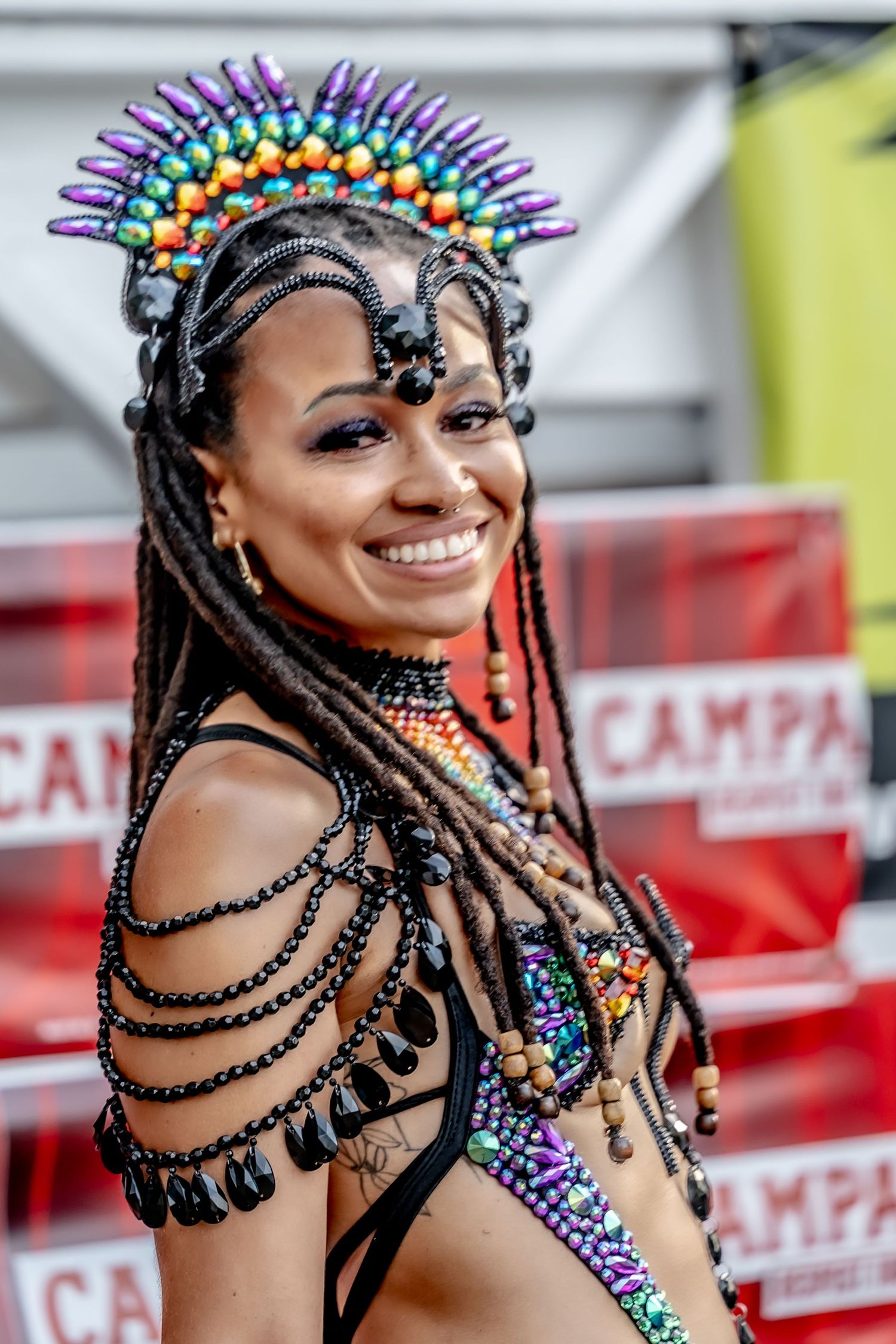 Smiling woman in colorful carnival costume with rainbow spiked headdress and black beaded jewelry at festival.