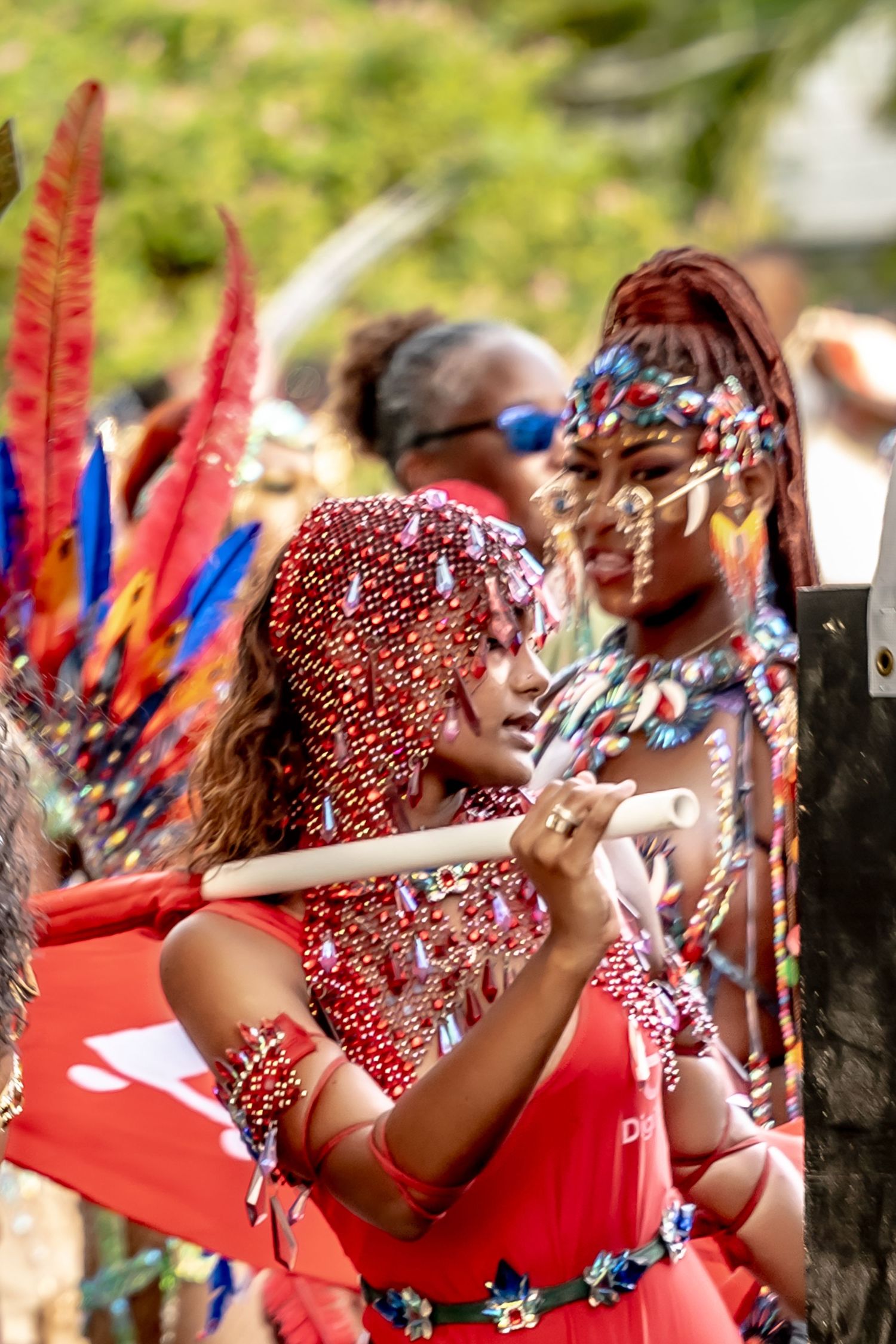 Women in vibrant beaded costumes and feathered headdresses perform at a colorful Caribbean carnival parade.
