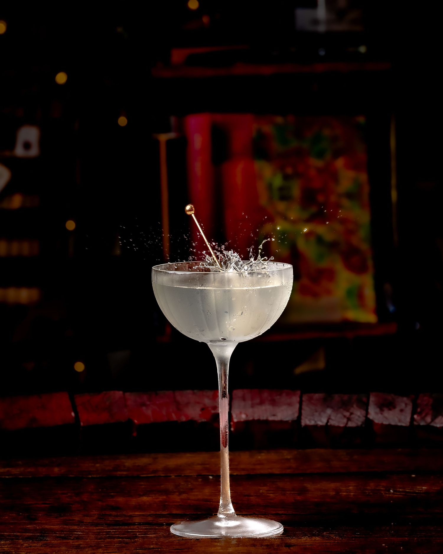 Elegant coupe cocktail glass with a splash effect on a dark wooden bar in a moody, dimly lit setting.
