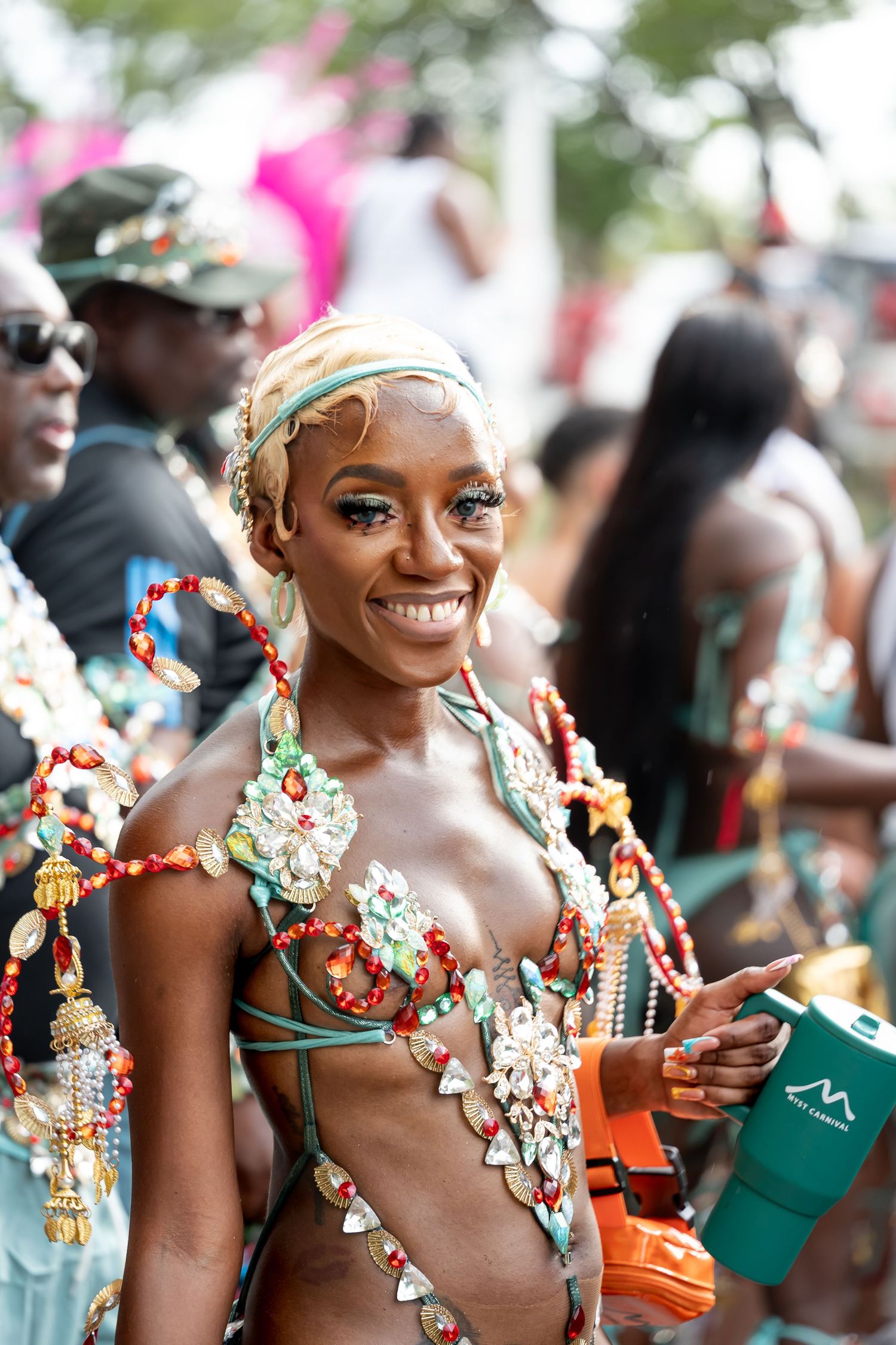 Smiling woman in colorful beaded carnival costume at a vibrant outdoor festival celebration.