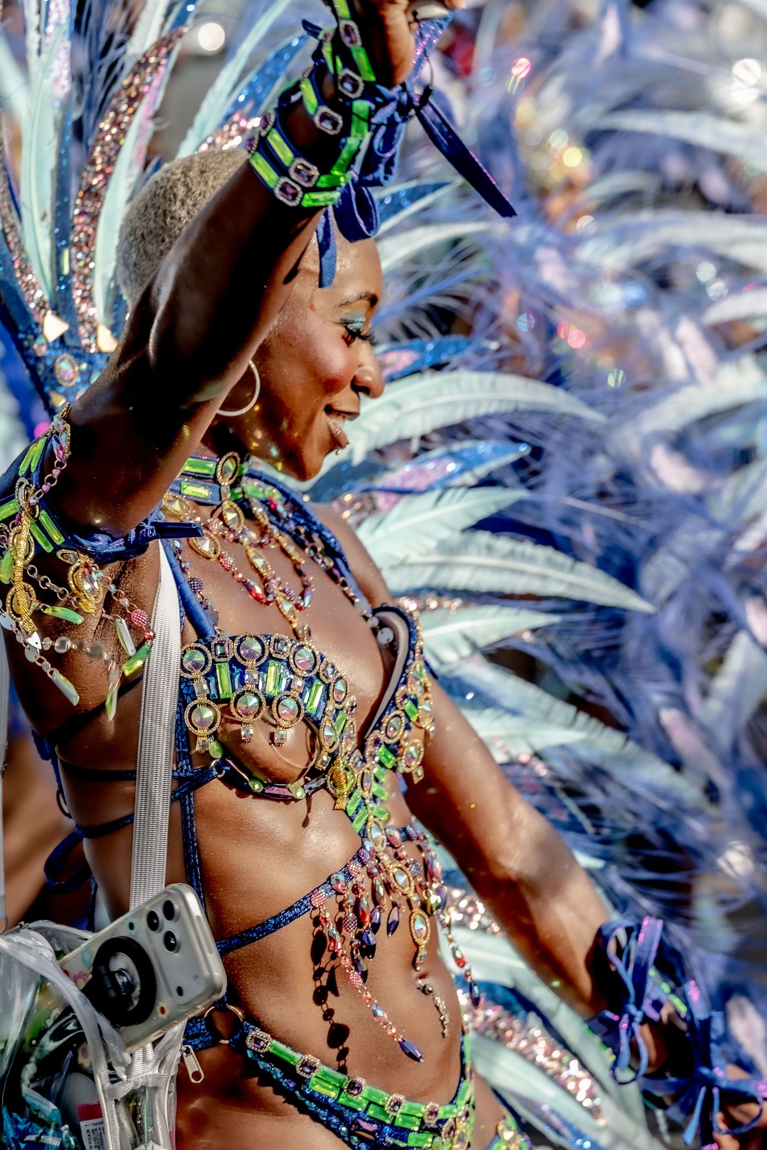Woman in vibrant beaded carnival costume with blue feathers dancing joyfully at a colorful festival parade.