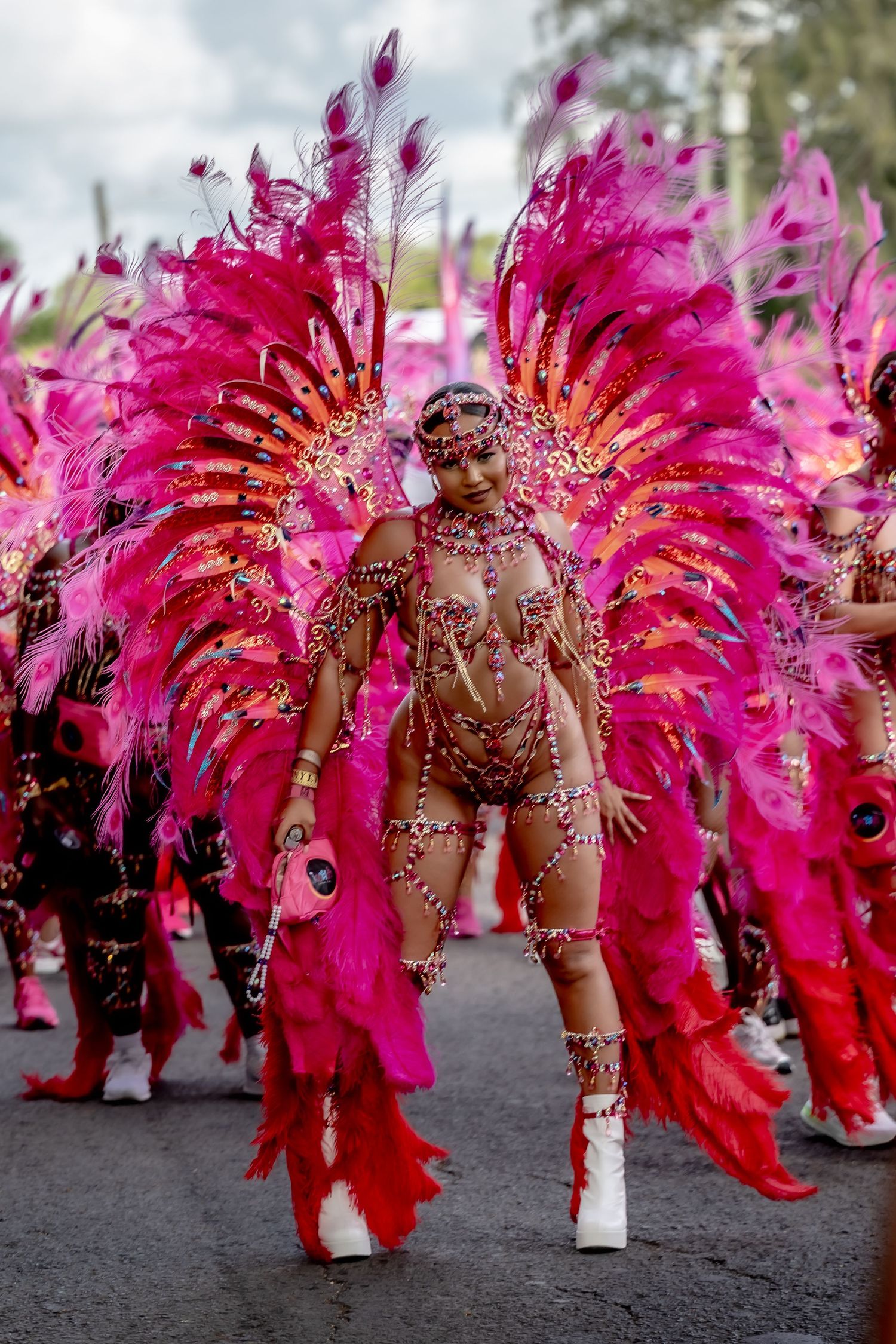 Vibrant carnival performer in stunning pink feather costume and jeweled bodysuit dancing at a festive parade celebration.