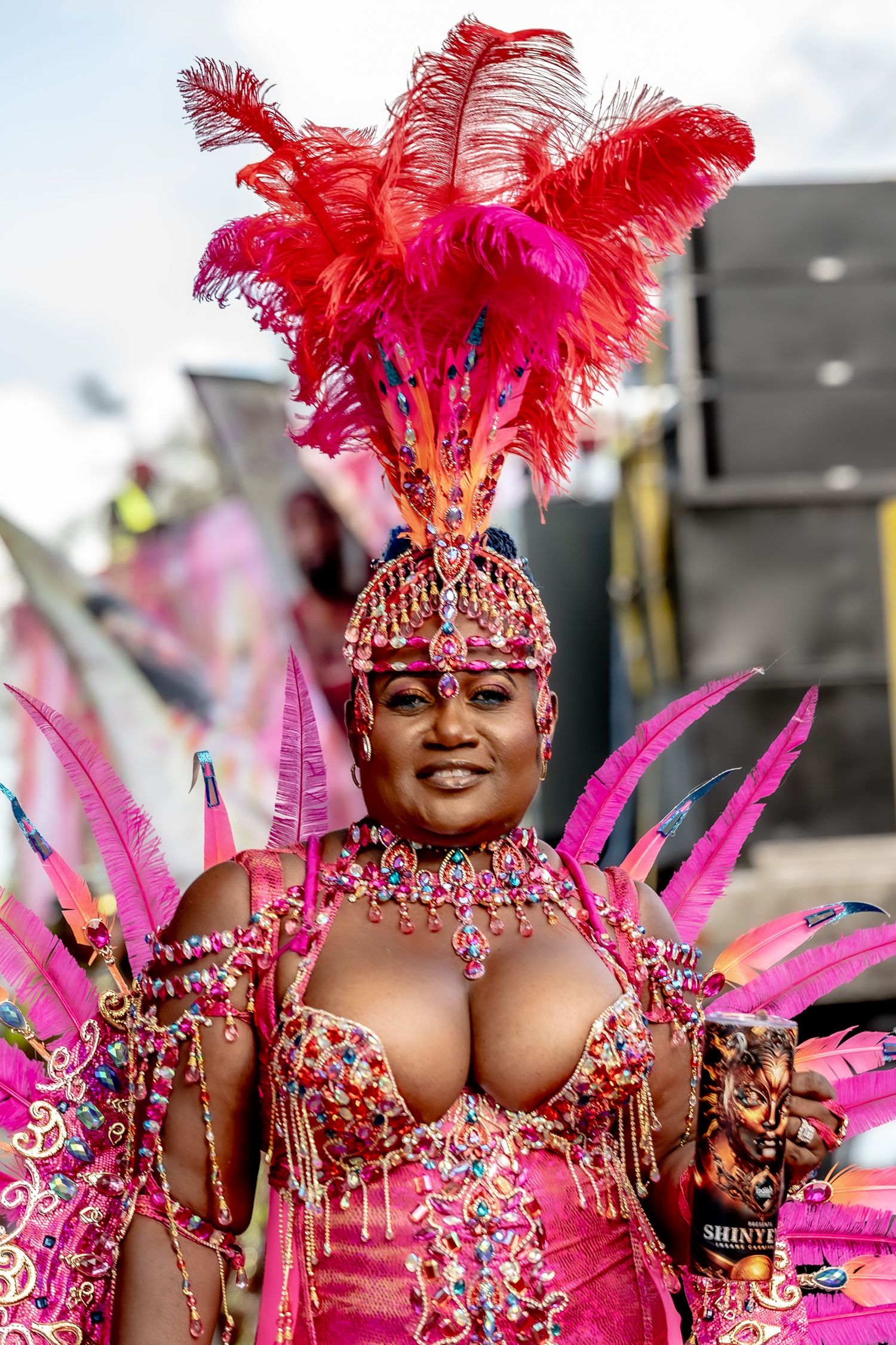 Woman in vibrant pink carnival costume with red feathers and jeweled headdress at a festive parade.