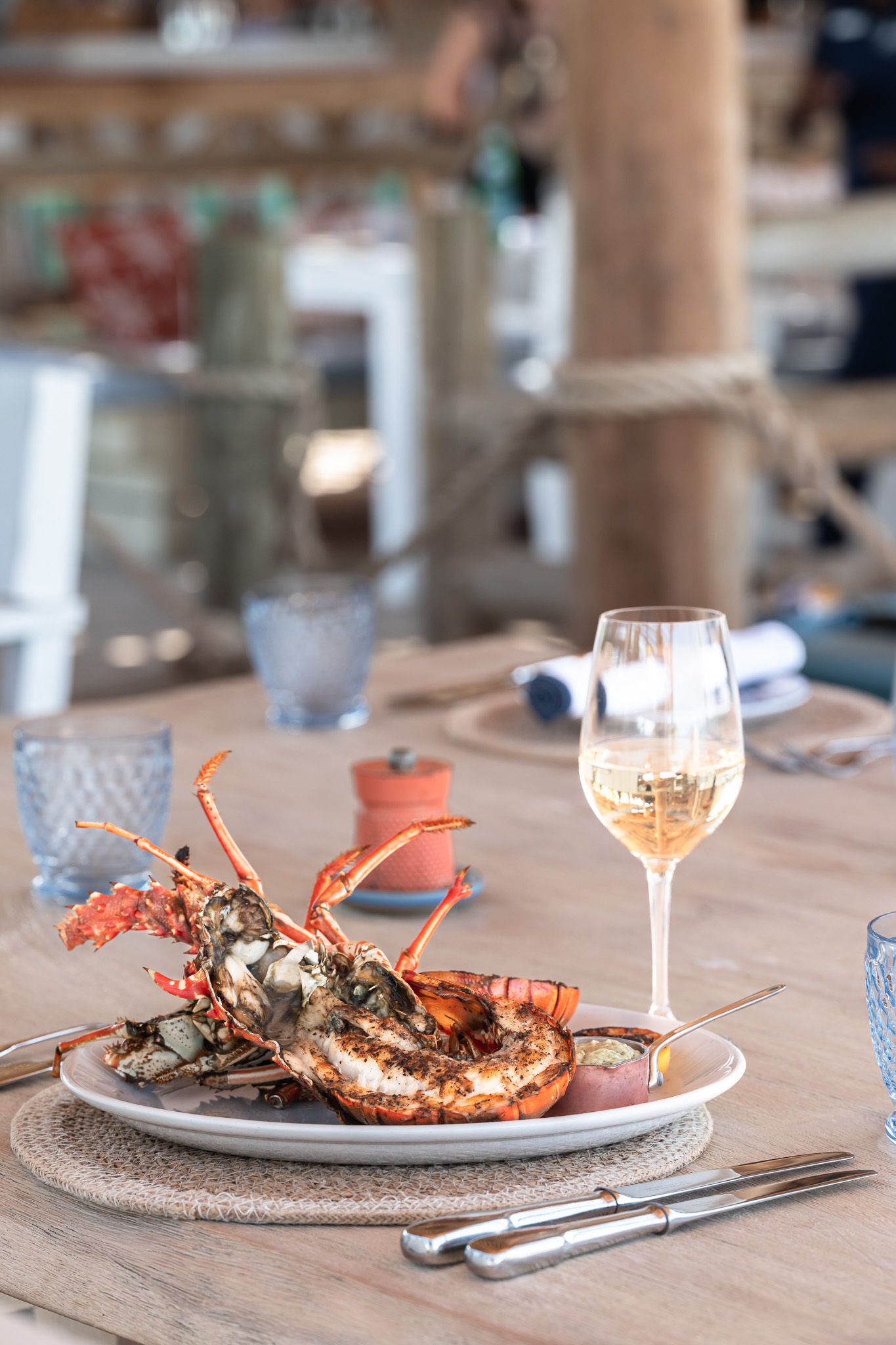 Grilled lobster tails served on white plates with wine glasses on a wooden table in a restaurant setting.