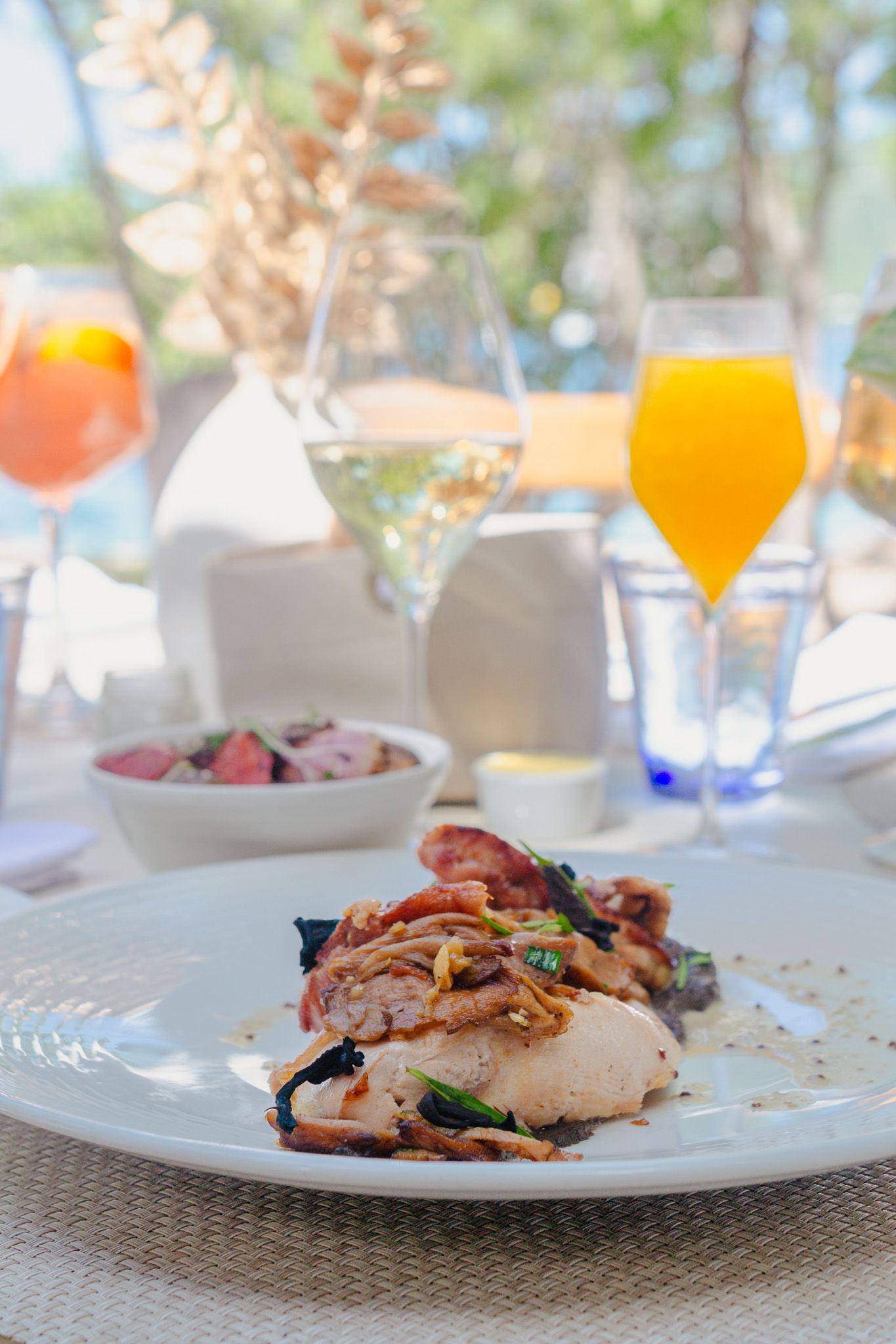 Elegantly plated chicken dishes with colorful garnishes and orange cocktails served on white plates in an upscale setting.